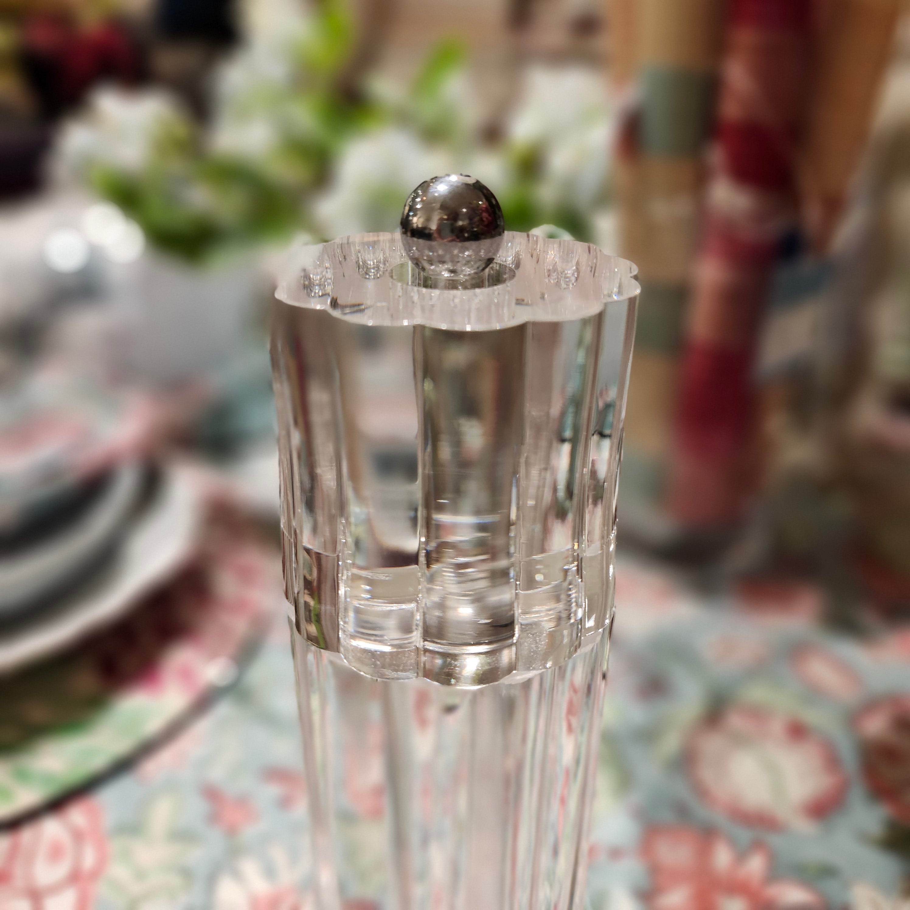 Clear glass salt or pepper grinder with silver top on a floral tablecloth