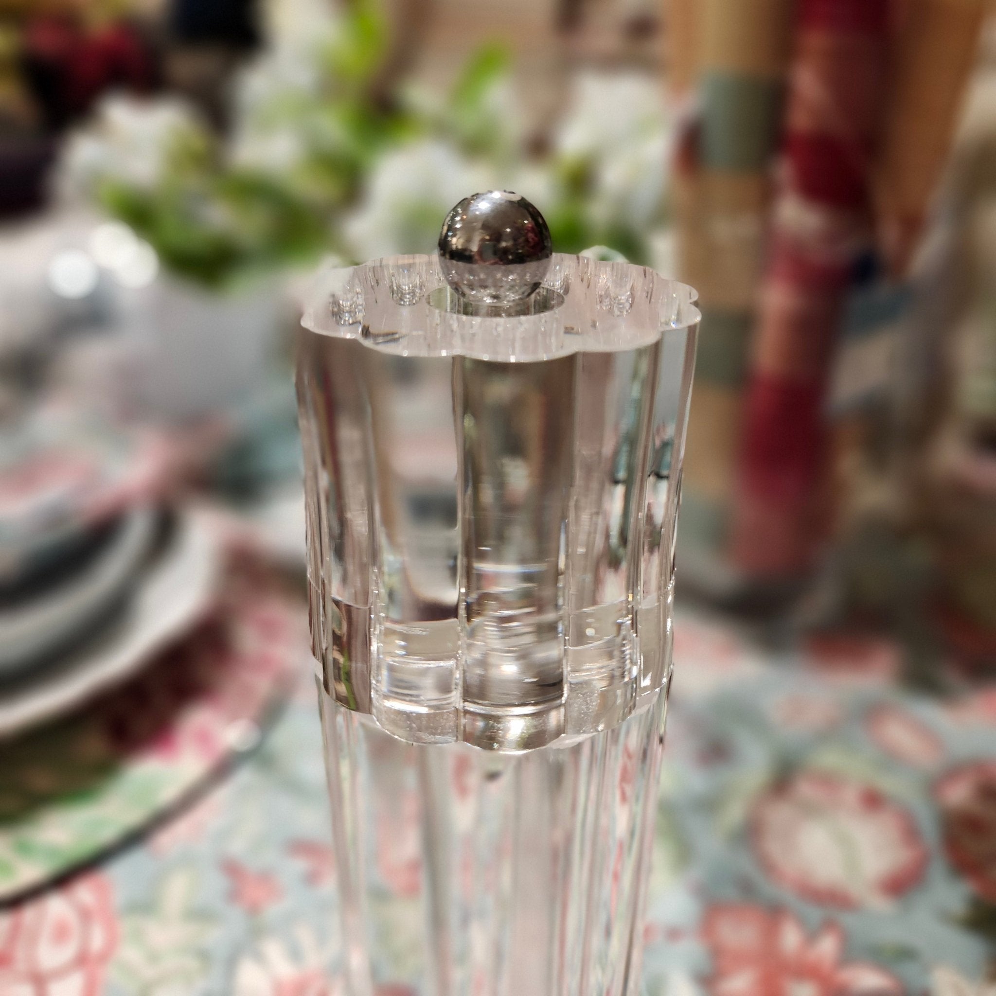 Clear glass salt or pepper grinder with silver top on a floral tablecloth