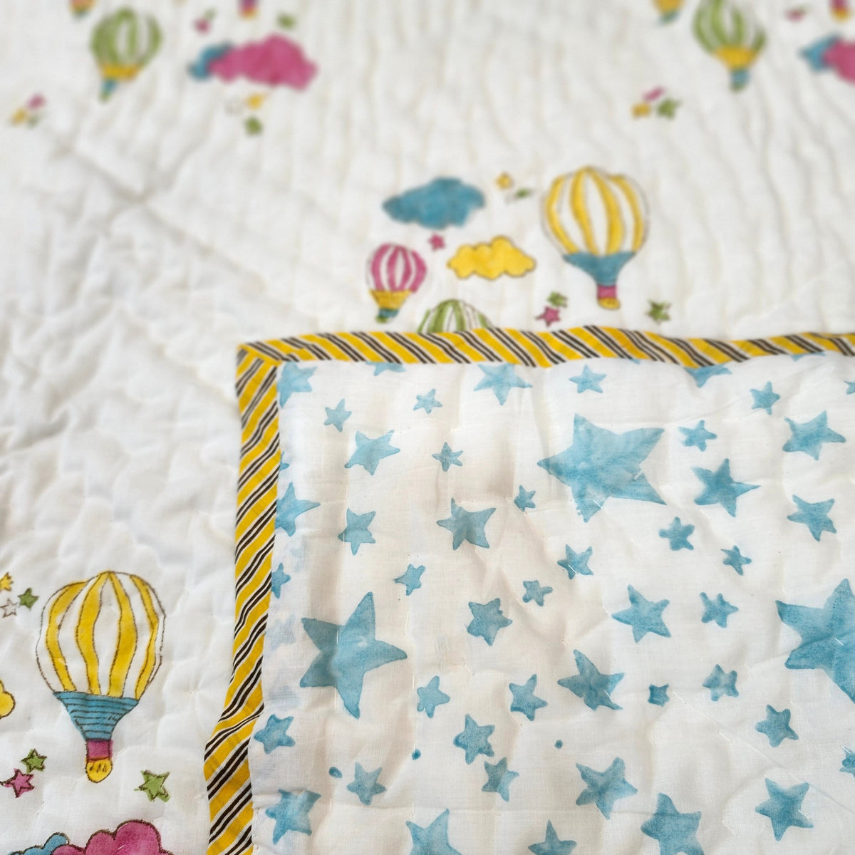 Child's hot air balloon print quilt folded back to show the reverse, blue stars on white, with a gold striped binding