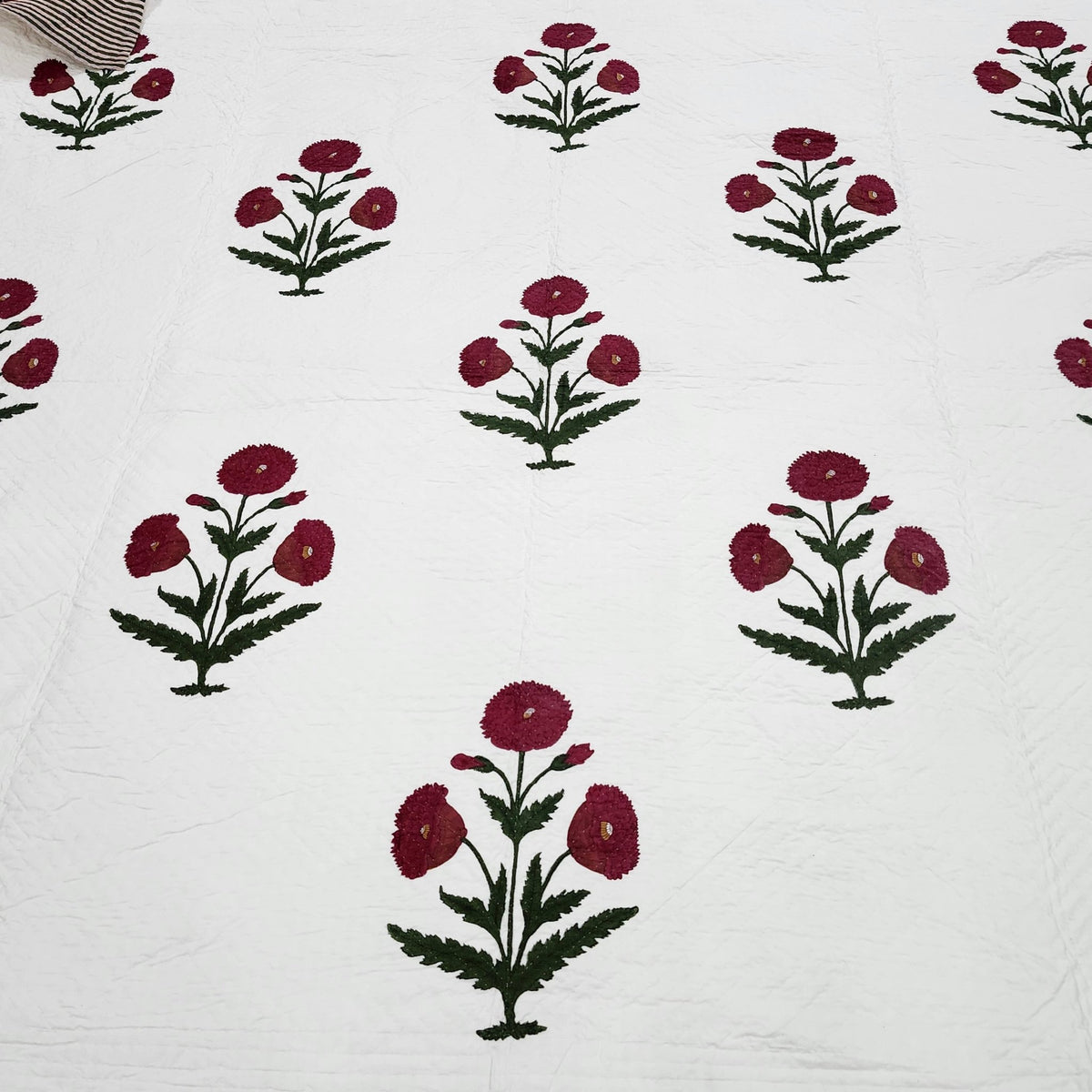 The king size poppy bedspread styled on a bed, 260 by 260cm, hand block printed and hand quilted.
