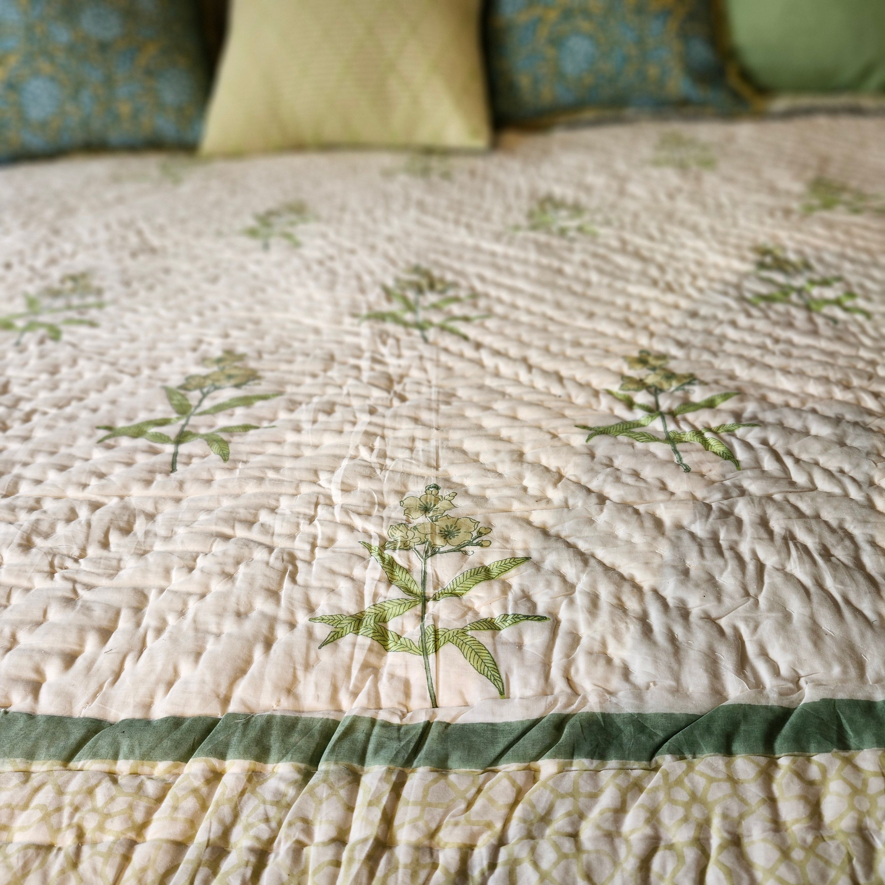 Close-up of a block print quilt with yellow flowers and green accents on a bed.