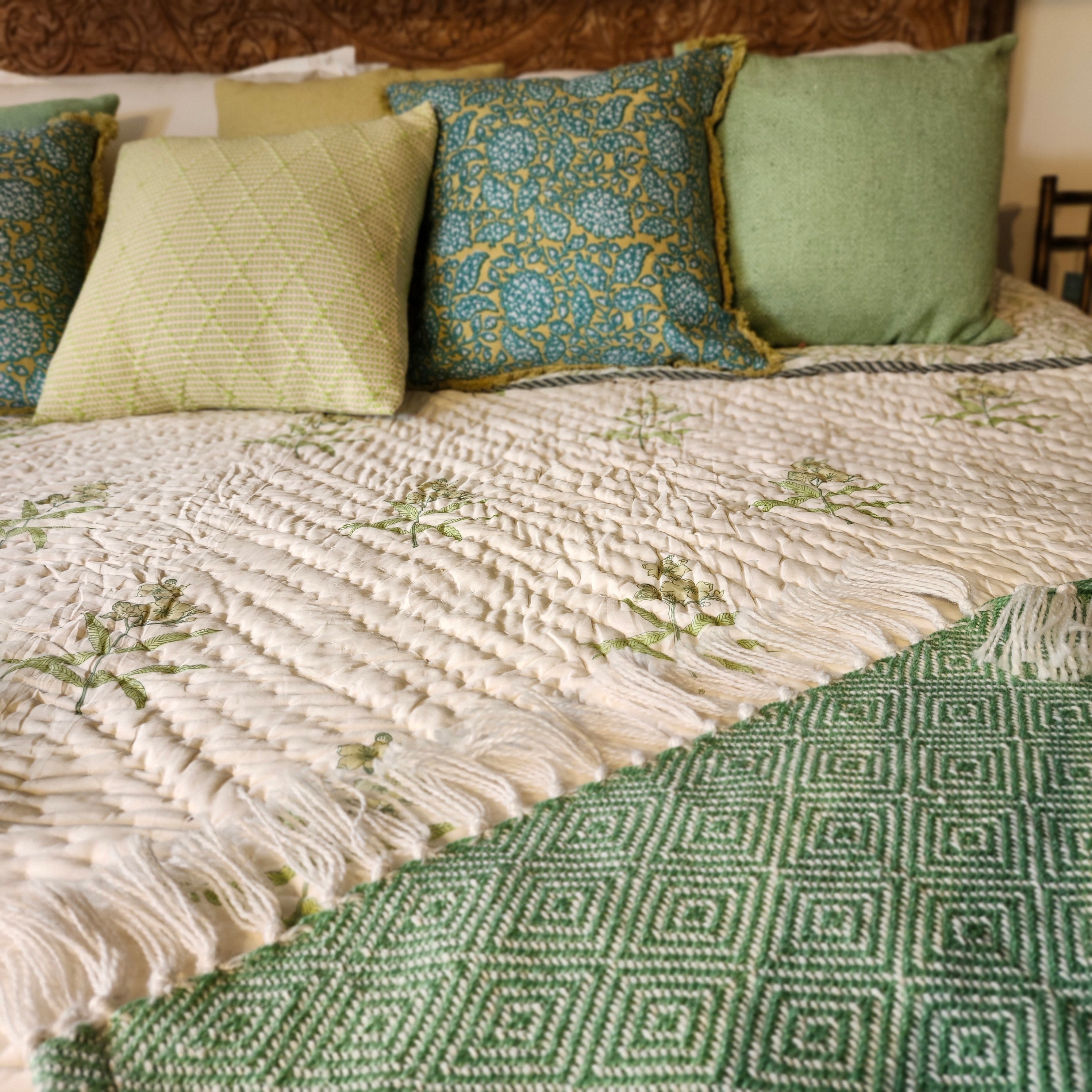 Close-up of a bed with yellow flowers block print quilt, cushions and a green throw