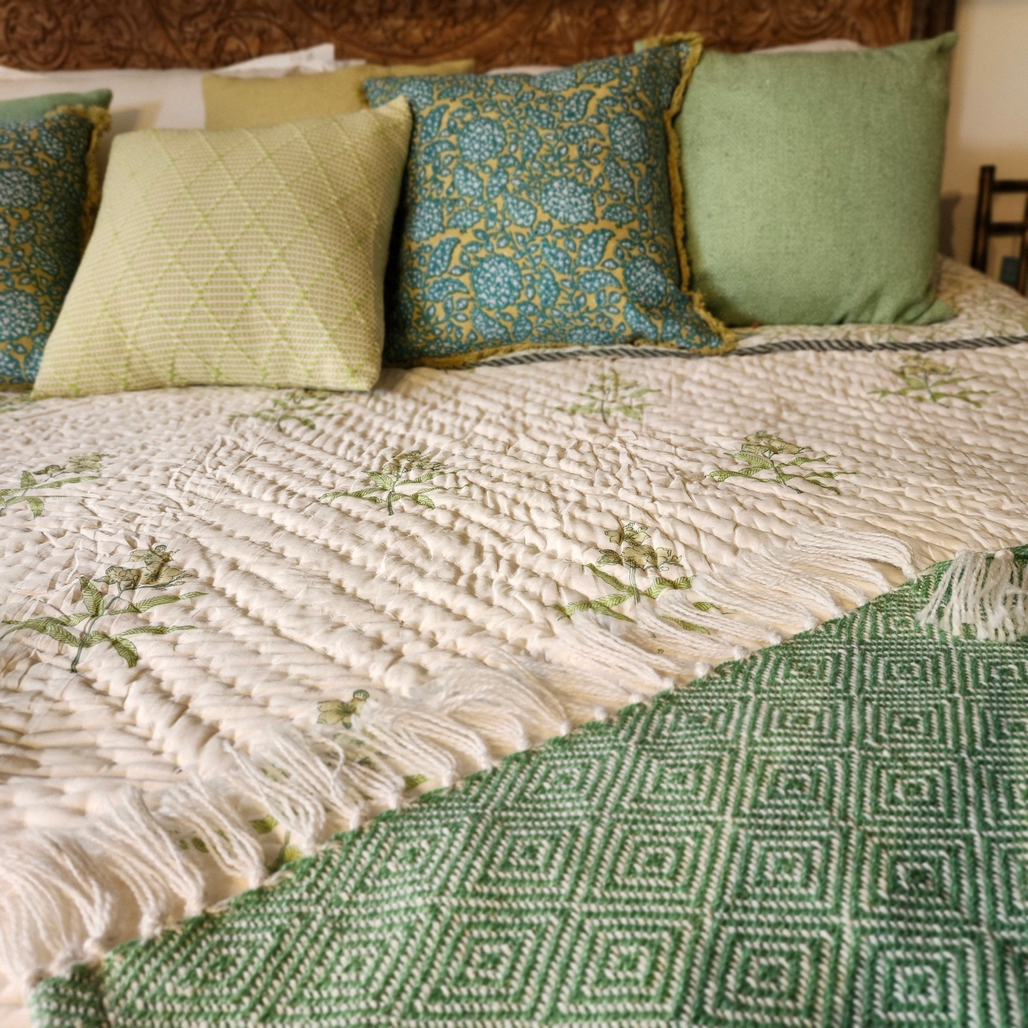 Close-up of a bed with yellow flowers block print quilt, cushions and a green throw