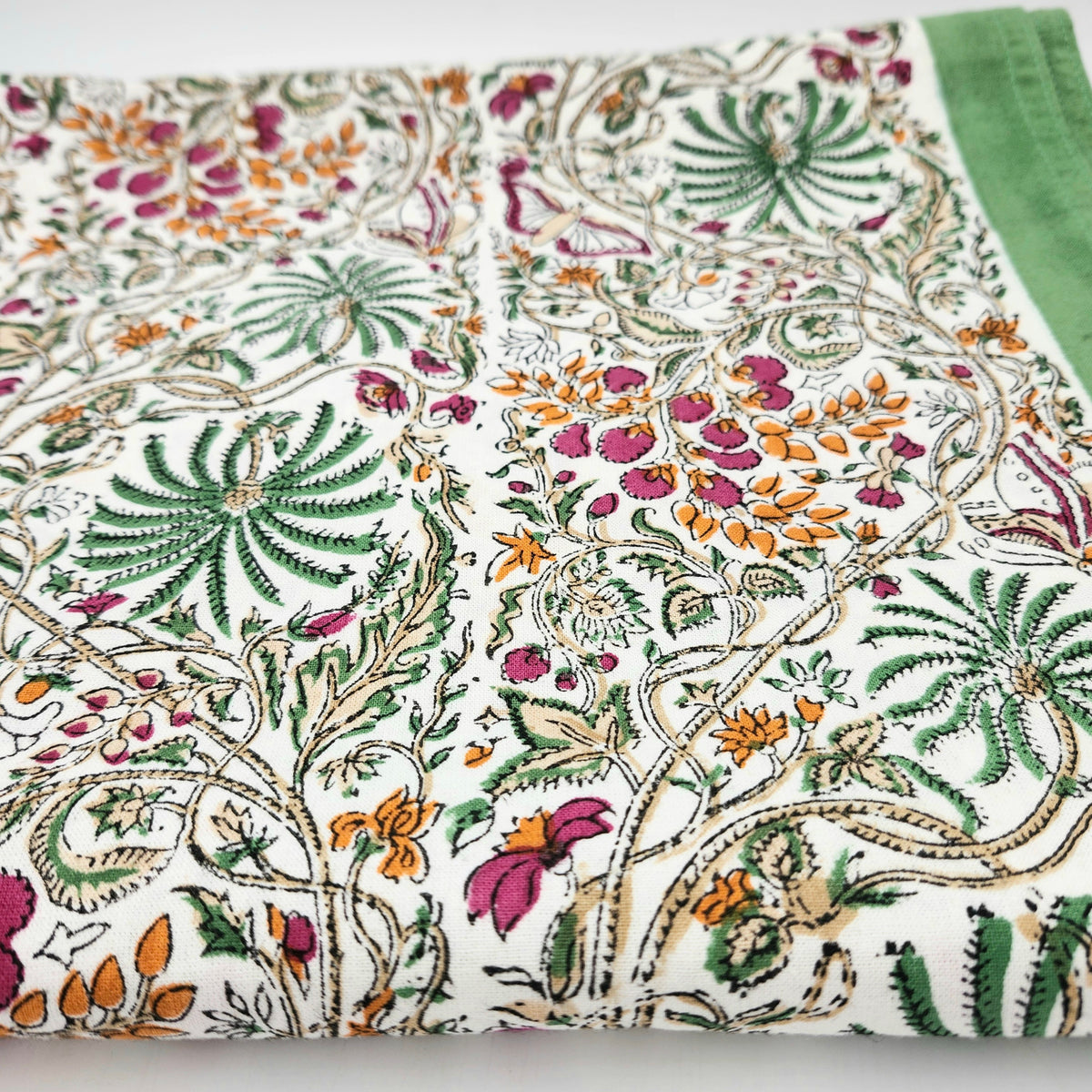 Multicoloured rainforest block-print cotton tablecloth with a green border, each colour added by hand