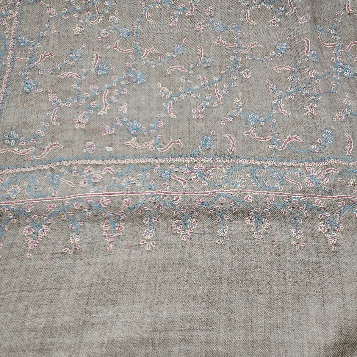 Detail of the fine pashmina shawl, hand embroidered in baby blue, pink and yellow on a natural ground.