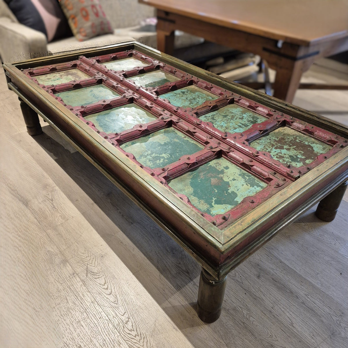 Detail of the red and aquamarine painted teak door under the solid glass top of a coffee table with four simply carved legs