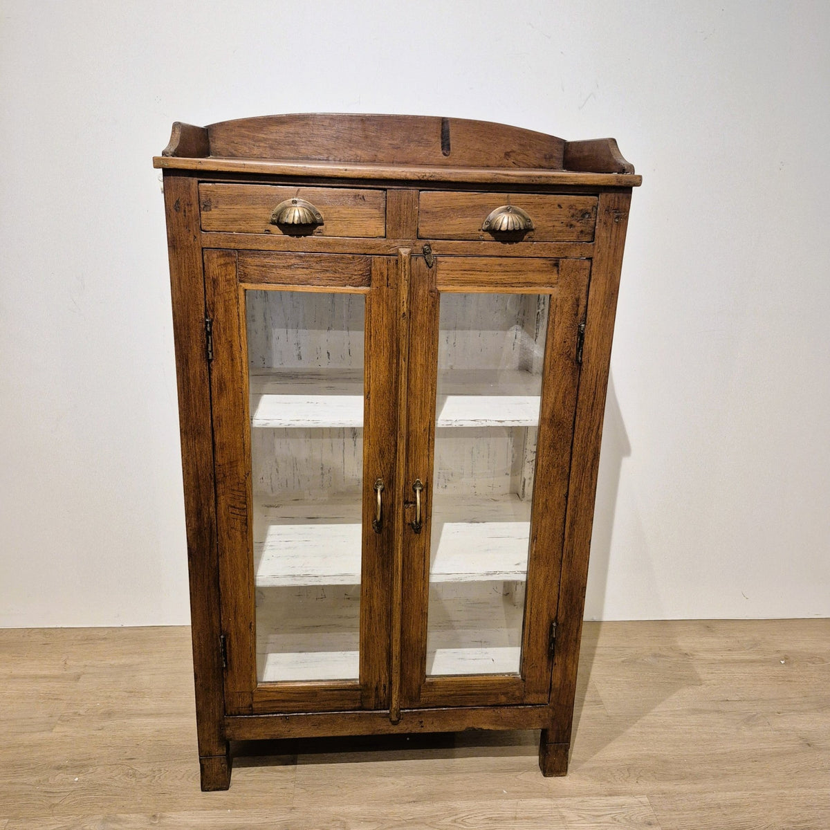 Small glass fronted teak cabinet with two brass handled drawers and three inner shelves, 125 cm high