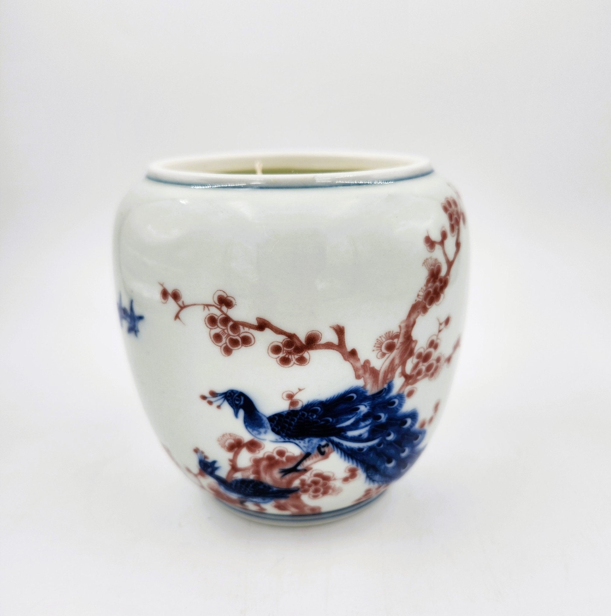 Scented Candle in a ceramic cup with blue peacocks and red blossom on a white background