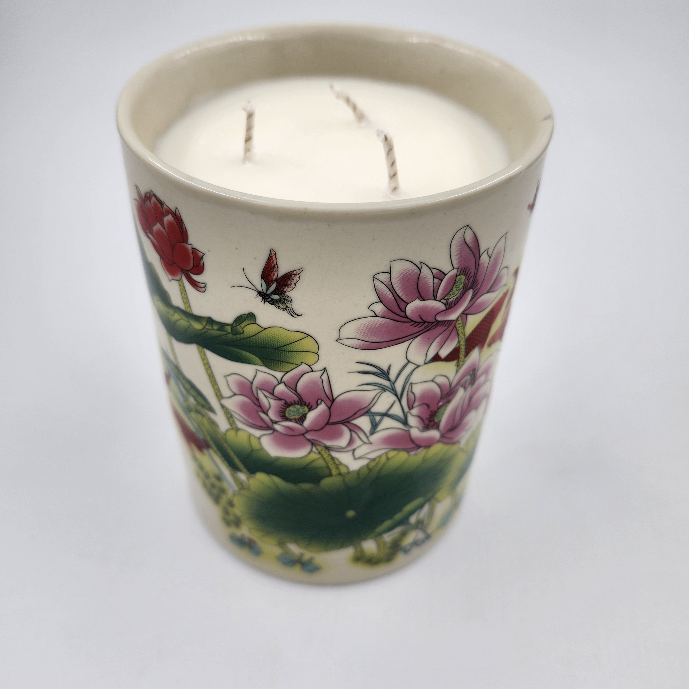 Candle in a decorative pot with floral and butterfly design on a white background