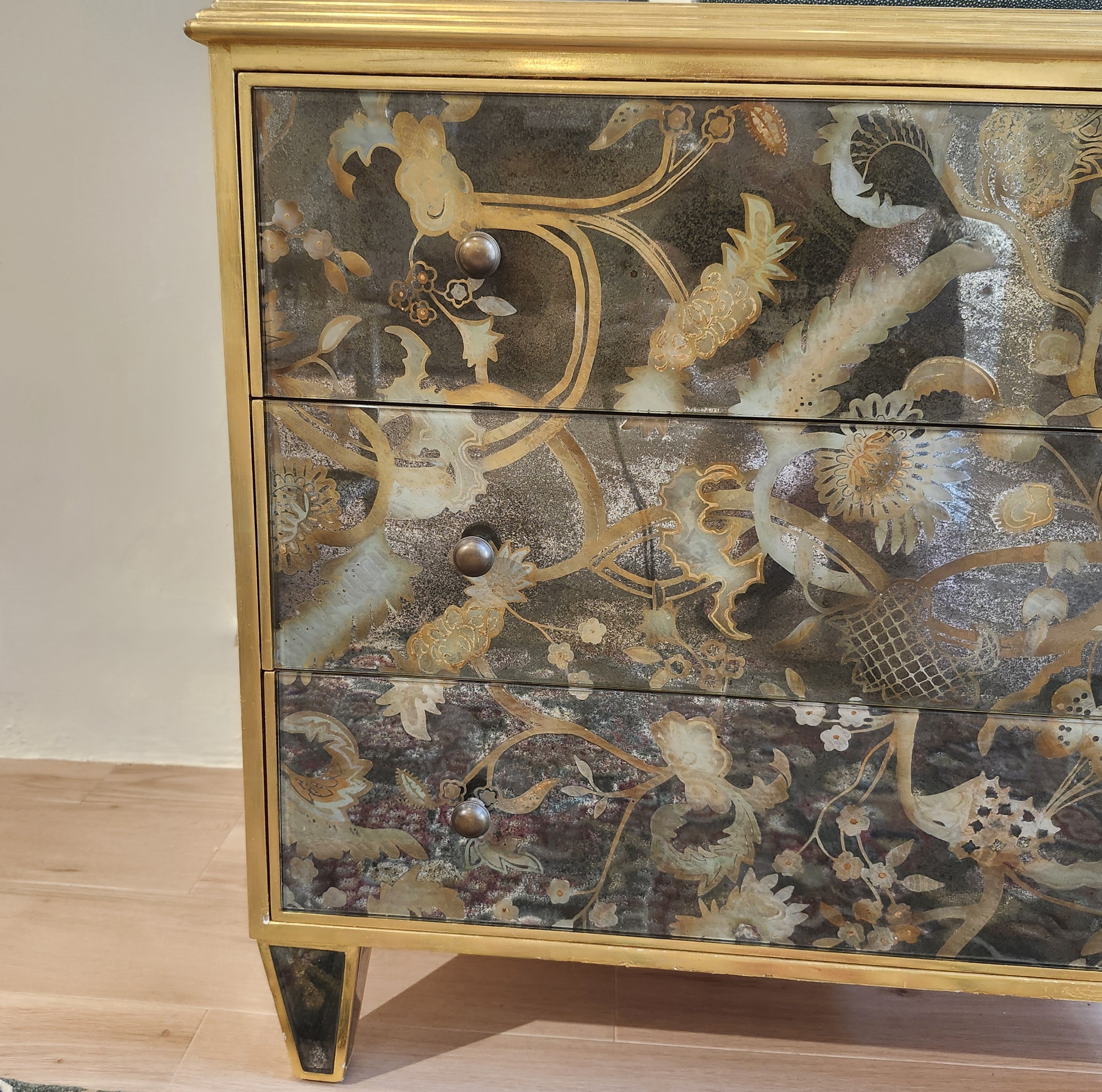 Églomisé chest of drawers with gold-leaf glass panels and antiqued brass knobs, styled view