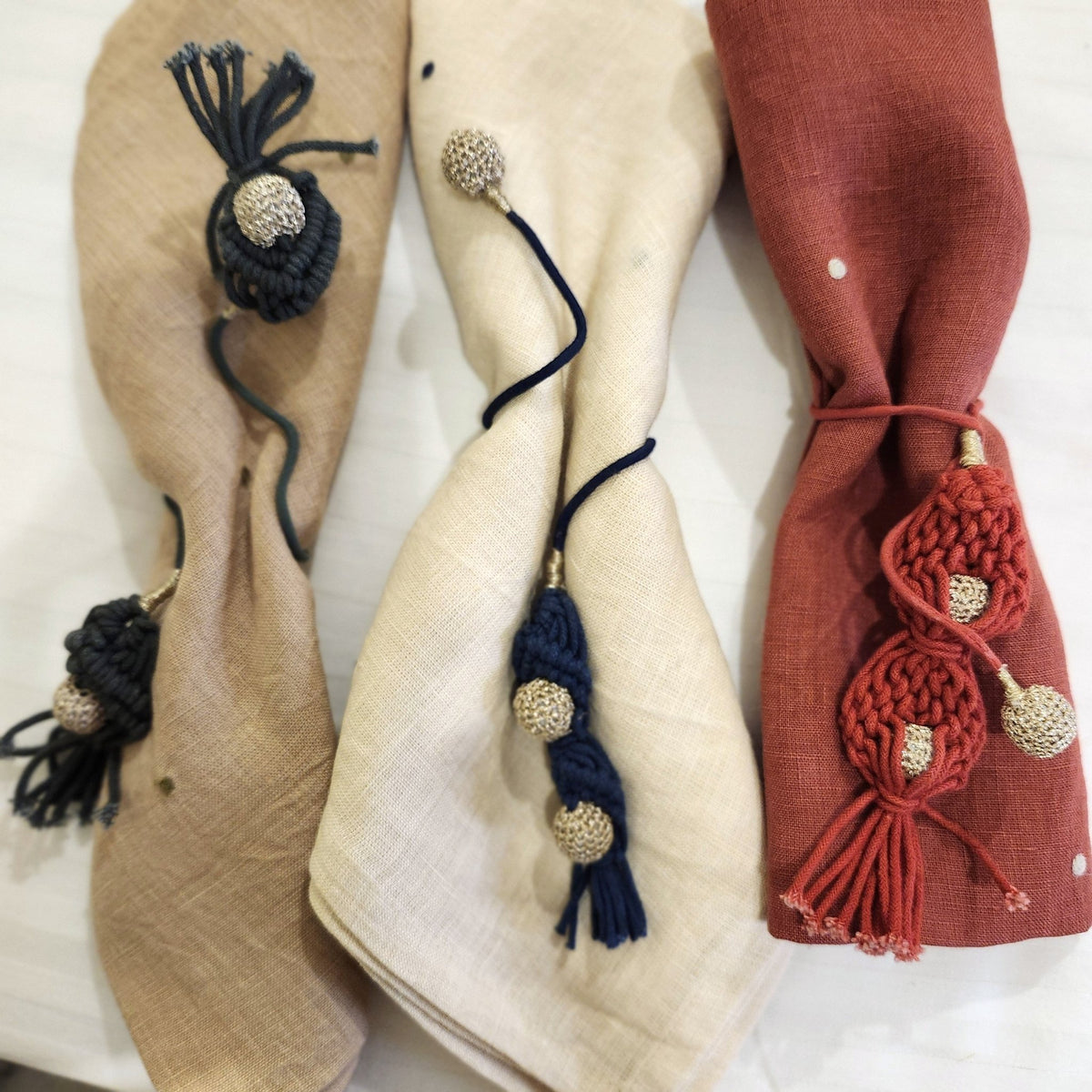 Set of six crochet napkin ties with metallic baubles at the ends, 30cm long, in red, sage and blue.