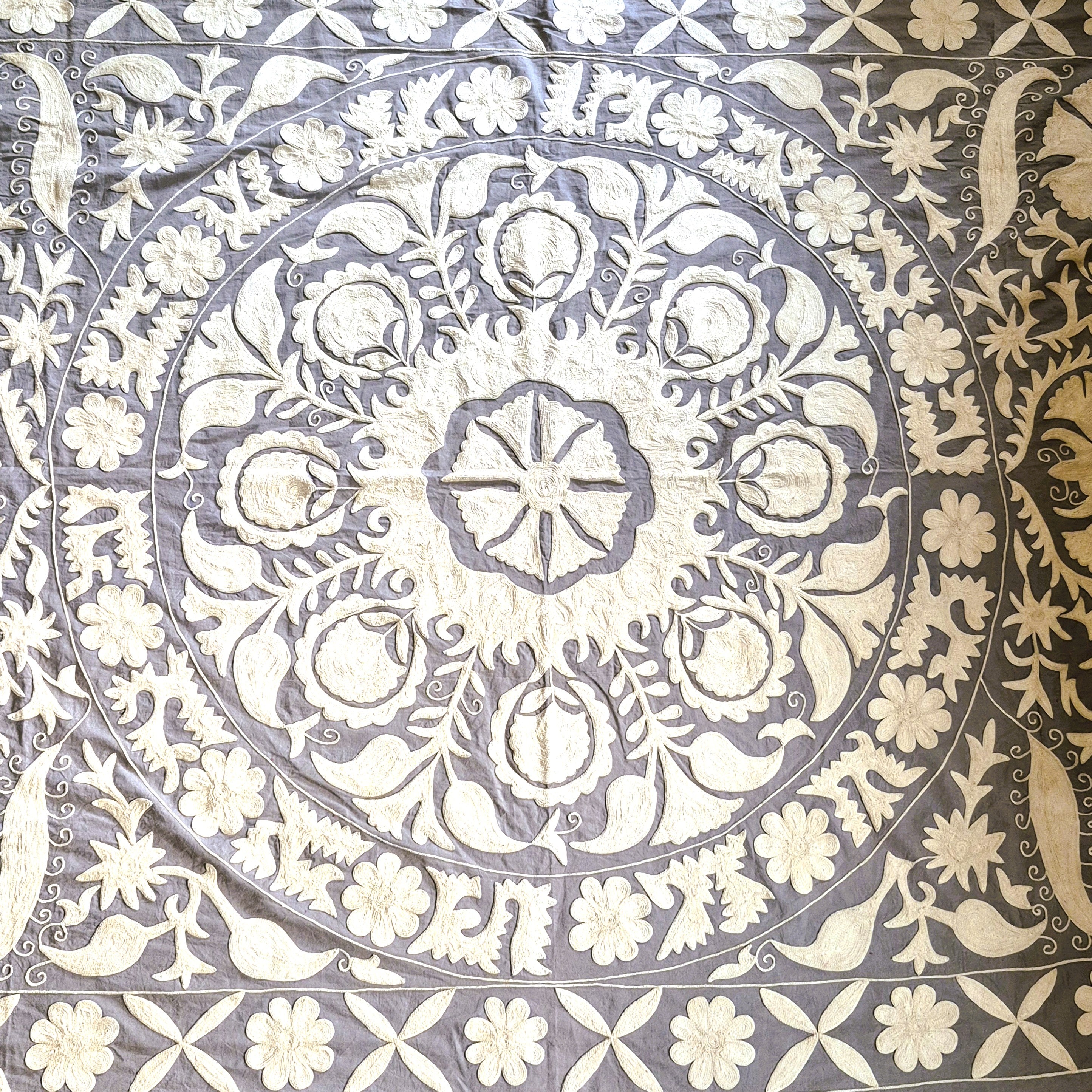 Hand embroidered suzani fabric with intricate white floral and geometric pattern on a gray background