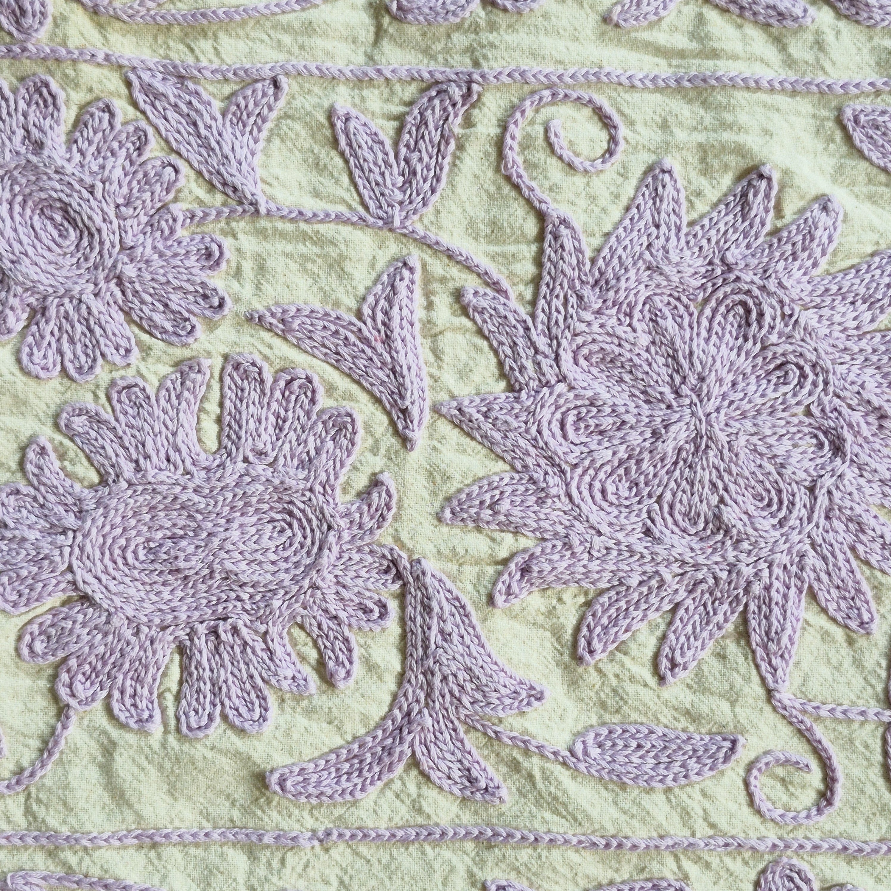 Detail of suzani throw showing lavender hand embroidery on a pale green cotton base, embroidered in India