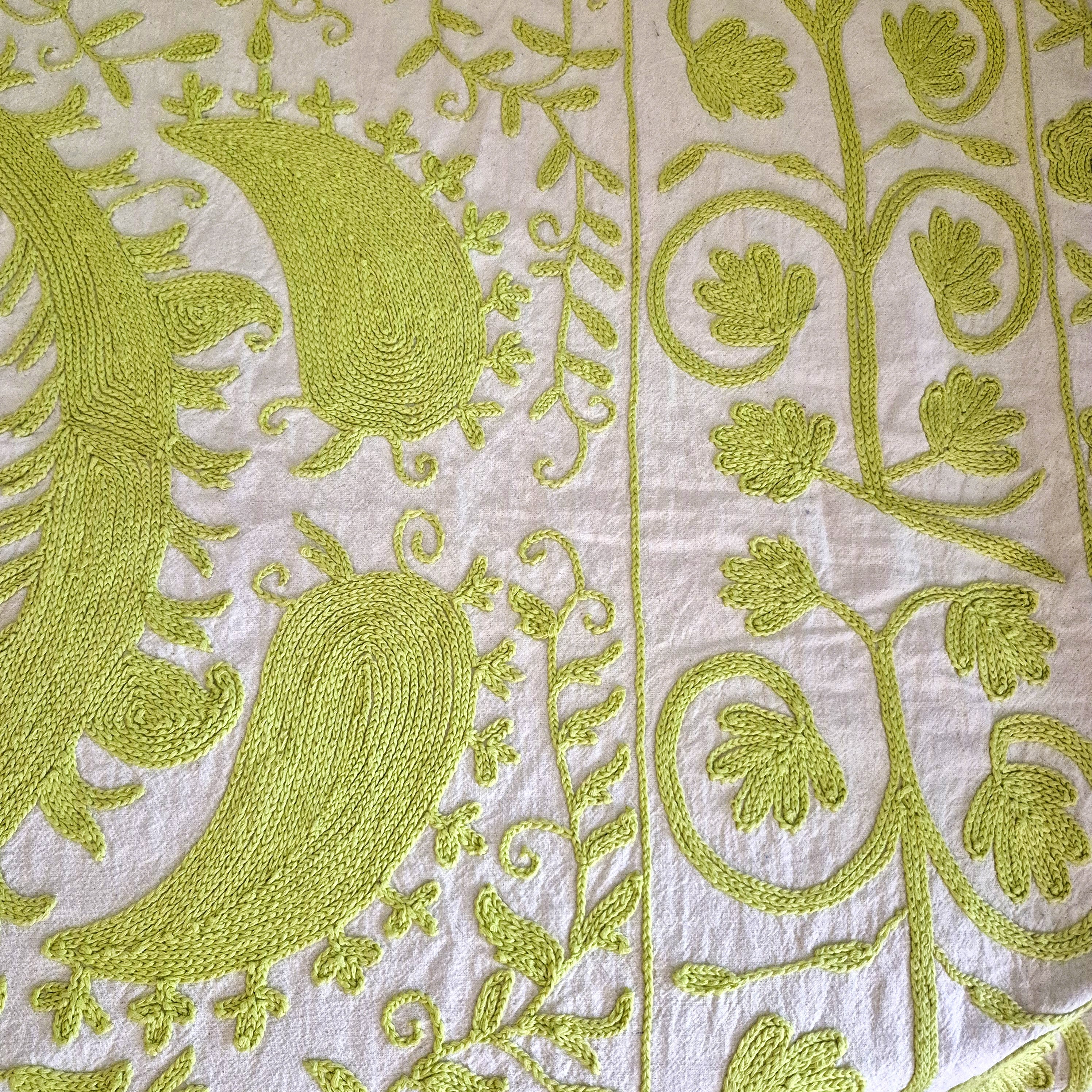 Close-up of lime green hand embroidered pattern on a cream fabric background. Suzani.