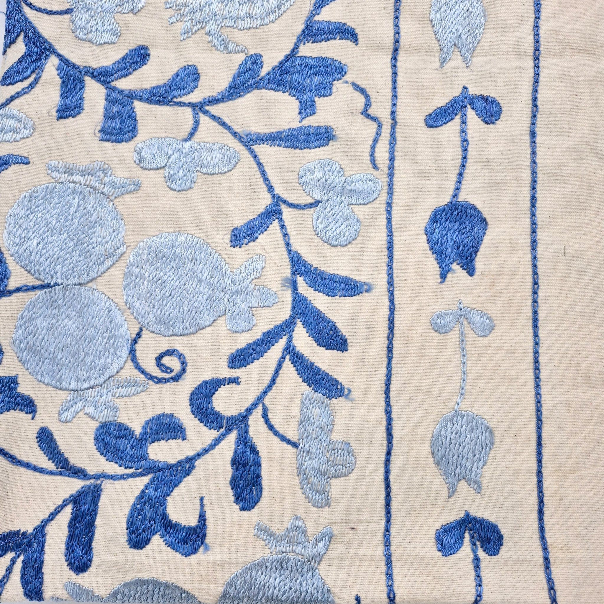 Close-up of suzani embroidered fabric with blue flowers and pomegranates on a cream background