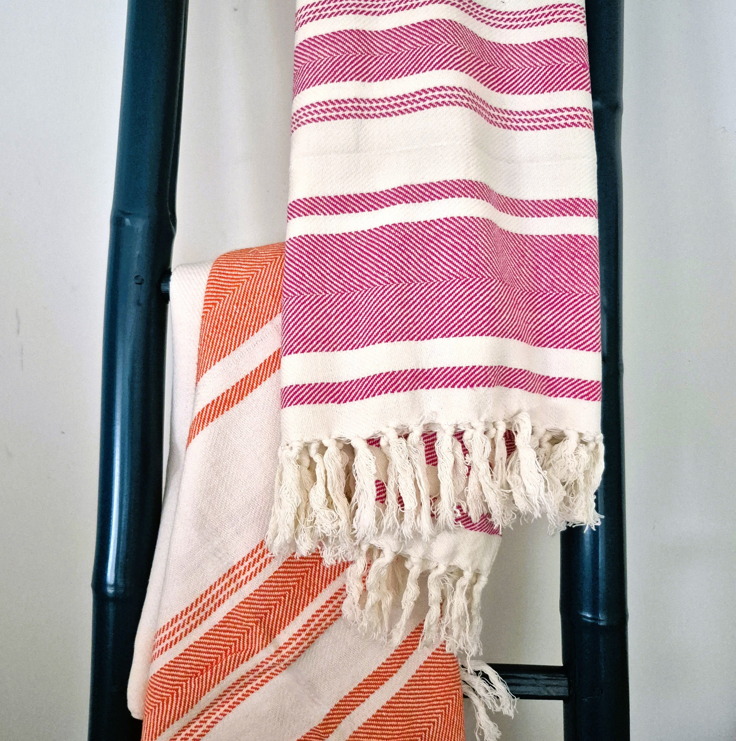 Striped towels in pink and orange draped over a towel ladder against a white background.