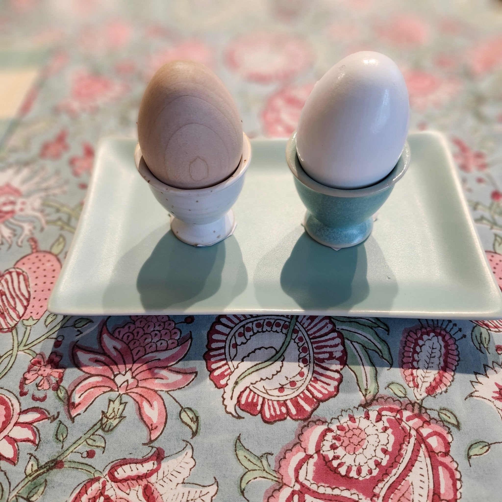 Ceramic egg cups in pastel colours arranged on a surface, styled