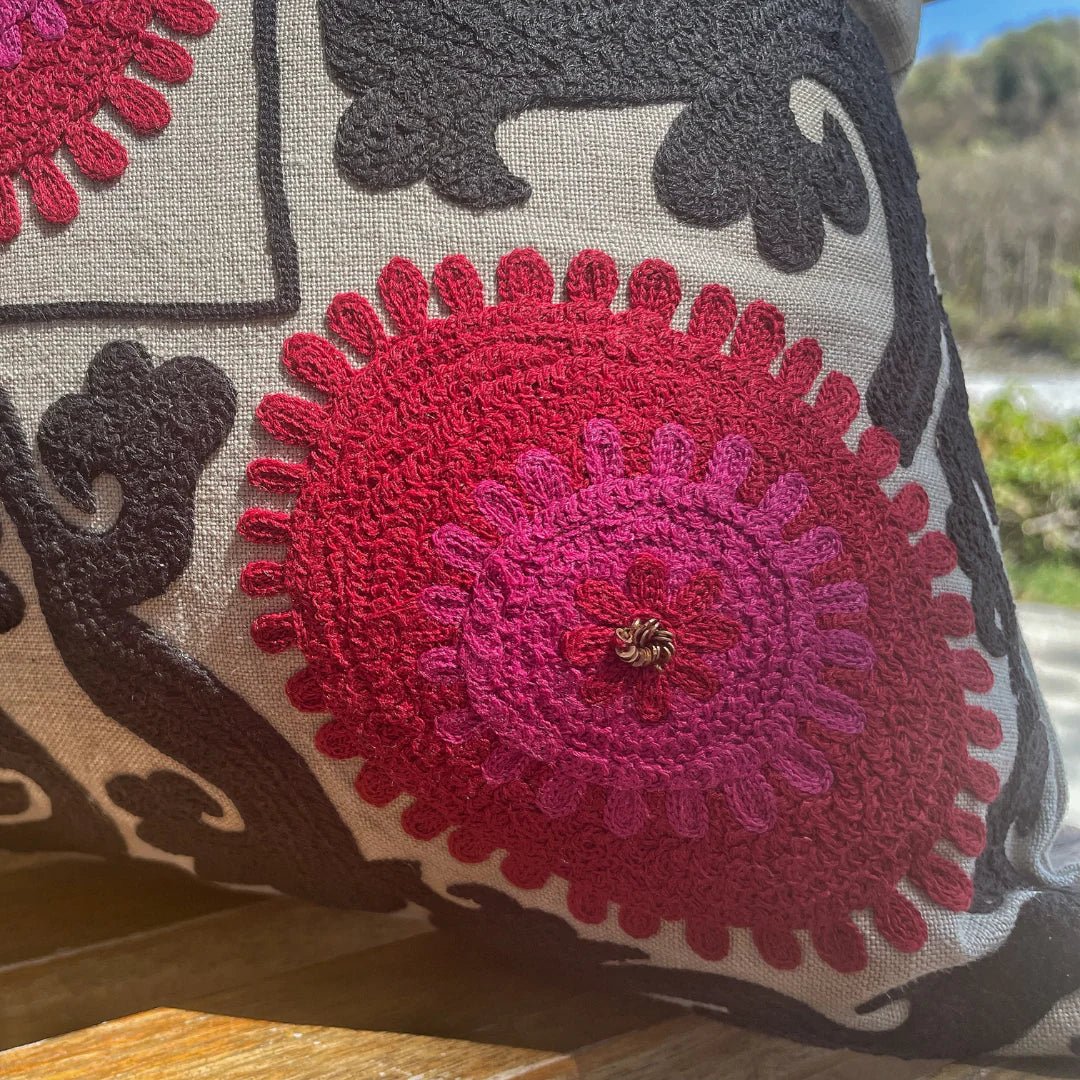 Close detail of the hand-embroidered Suzani linen cushion in red, pink and black with metalwork stitching, 35 by 50 cm