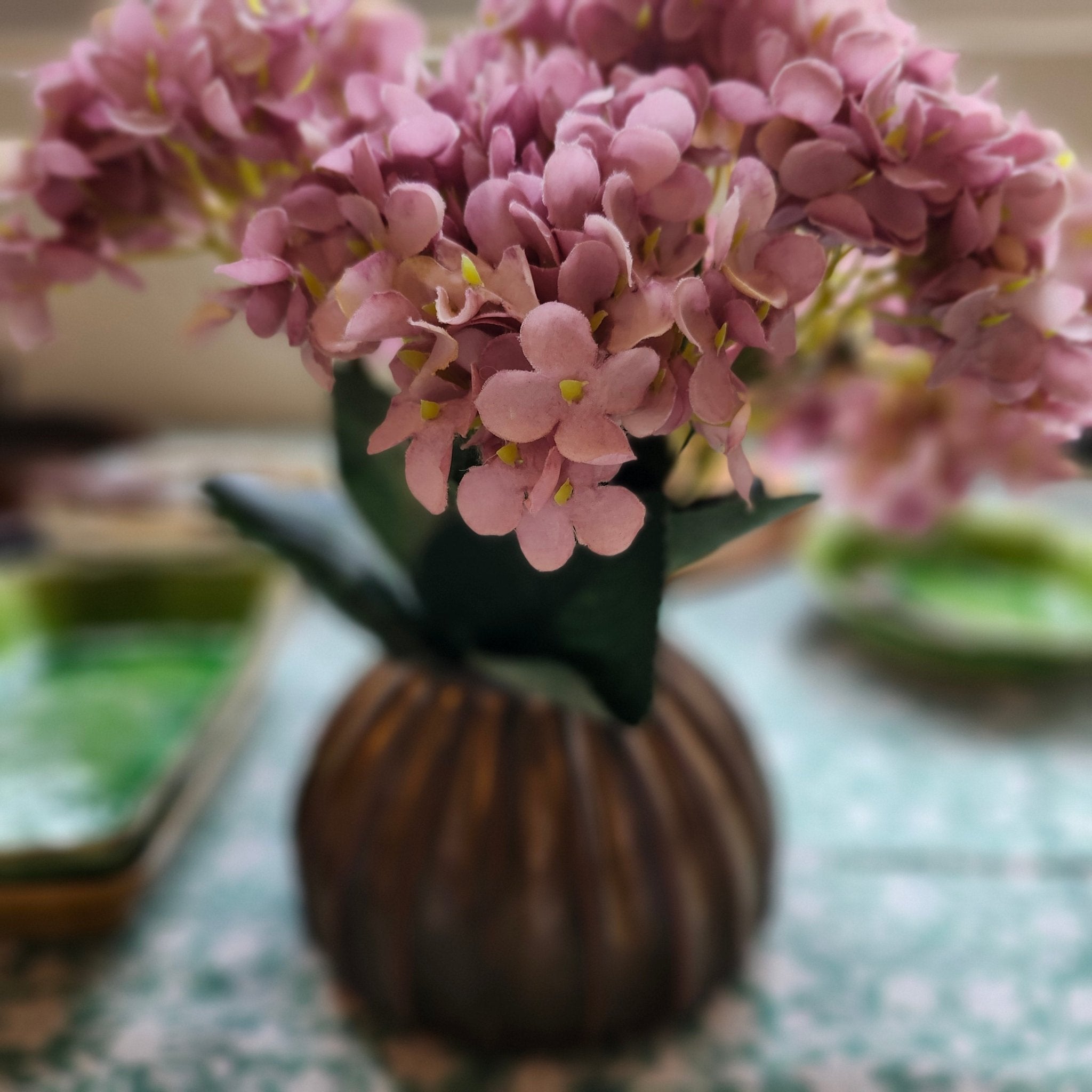A close-up of pink hydrangea flower heads with green leaves, photographed in a real indoor setting 