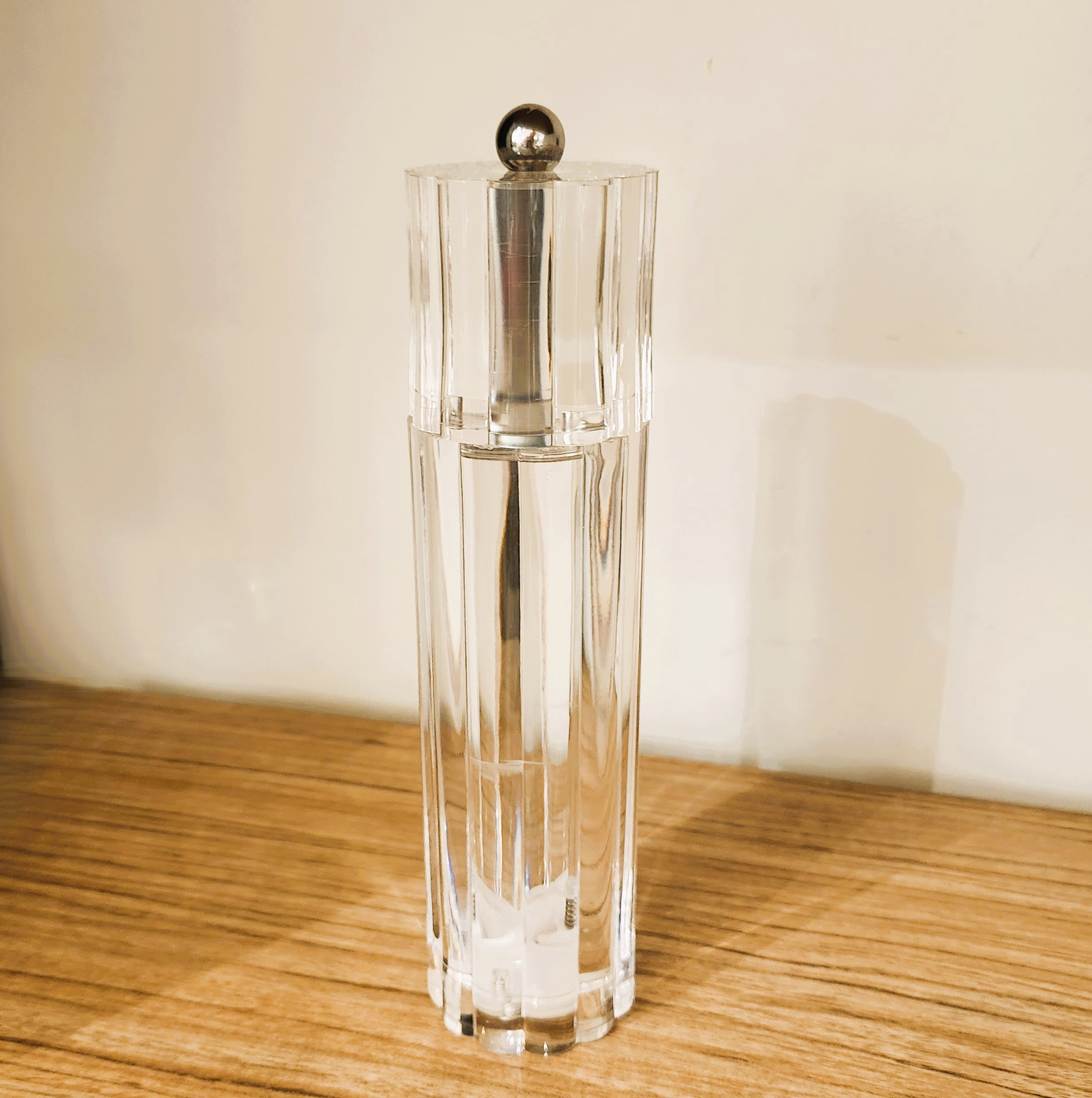 Clear acrylic salt or pepper grinder with silver top on a wooden surface