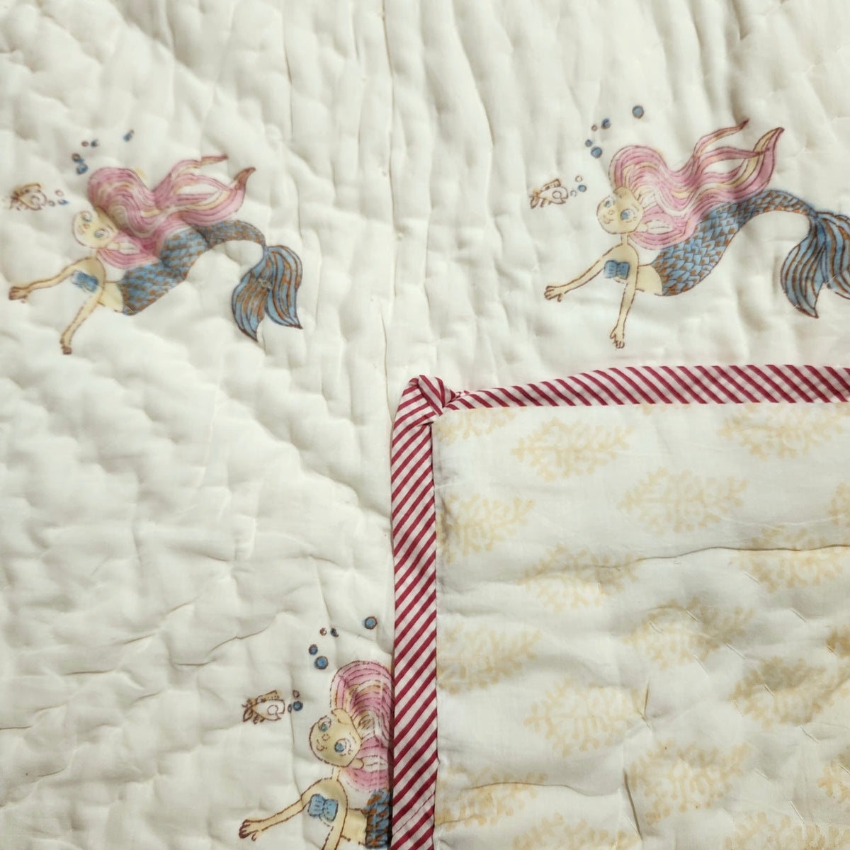 Detail of the mermaid child's quilt, with a contrast pattern in yellow on the reverse, reversible and machine washable warm
