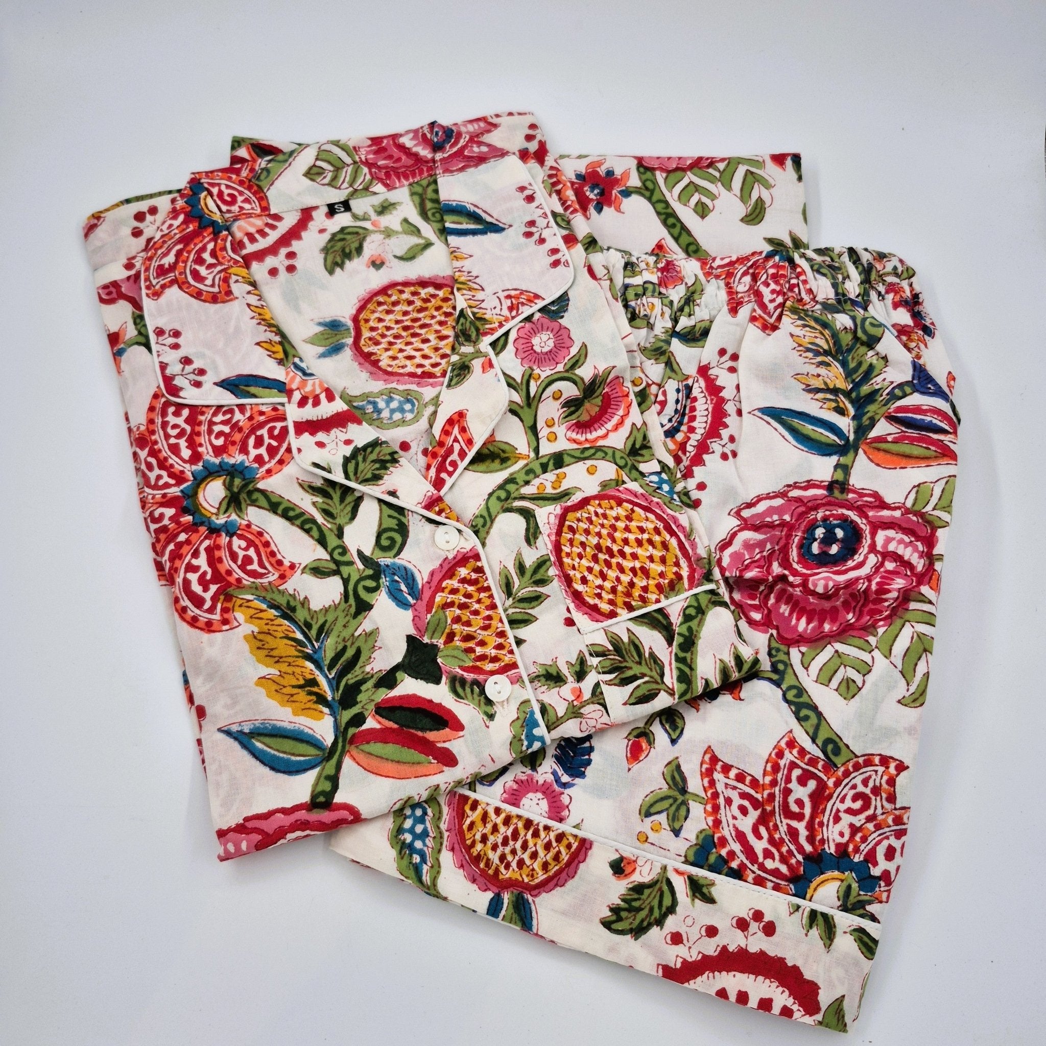Short pyjamas with a vibrant hand-block print featuring pink flowers, red and orange pomegranates, and green leaves on a cream background.
