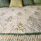 Close-up of a block print quilt with yellow flowers and green accents on a bed.