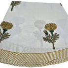 A round block printed poppy tablecloth with mustard yellow flowers and striped border