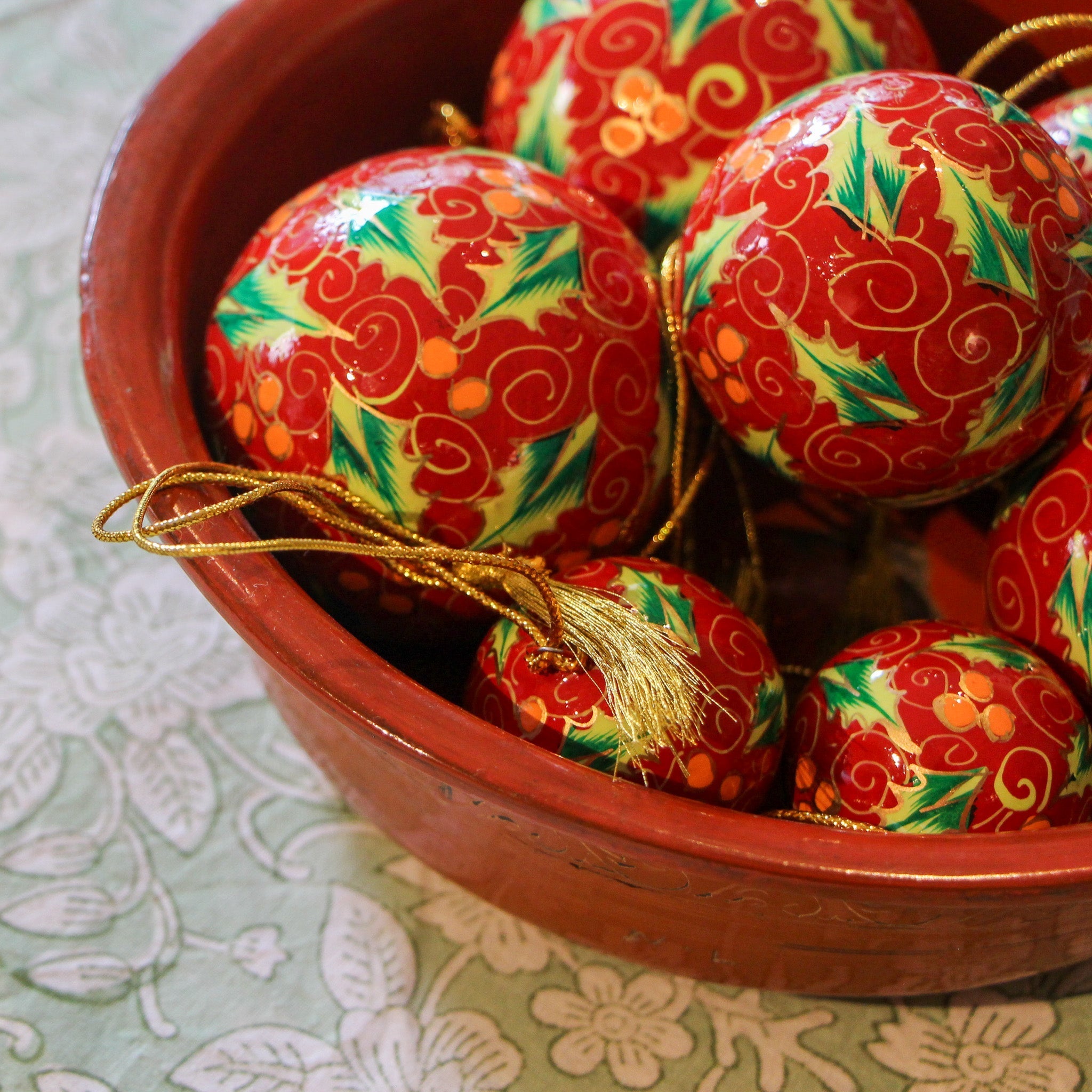 Red papier-mache Christmas bauble hand-painted with holly leaves and berries