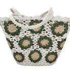 A crocheted tote bag with white lace-like crochet and green floral motifs outlined with beige centers, shown on a plain white background.