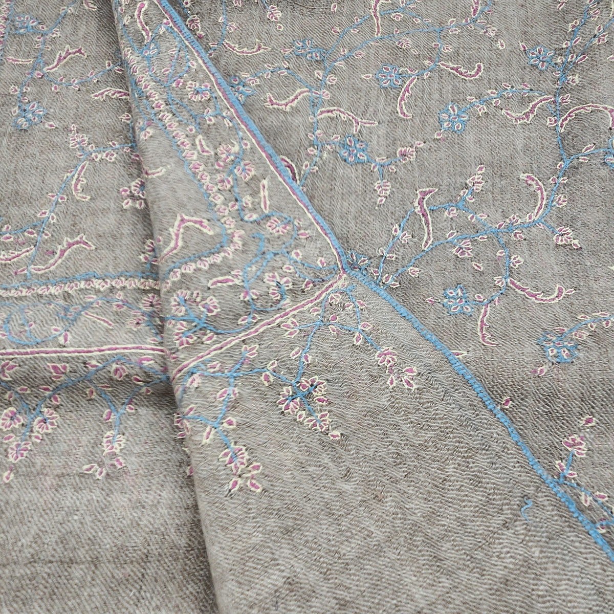 Hand-embroidered pashmina shawl with baby blue, pink and yellow floral threads on a natural background.