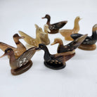A group of horn duck shaped chopstick stands in various shades of brown, black, and tan, arranged on a plain white background.