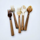 Five horn and wood pieces of cutlery, including three dessert forks, and two spoons, arranged on a plain white background.