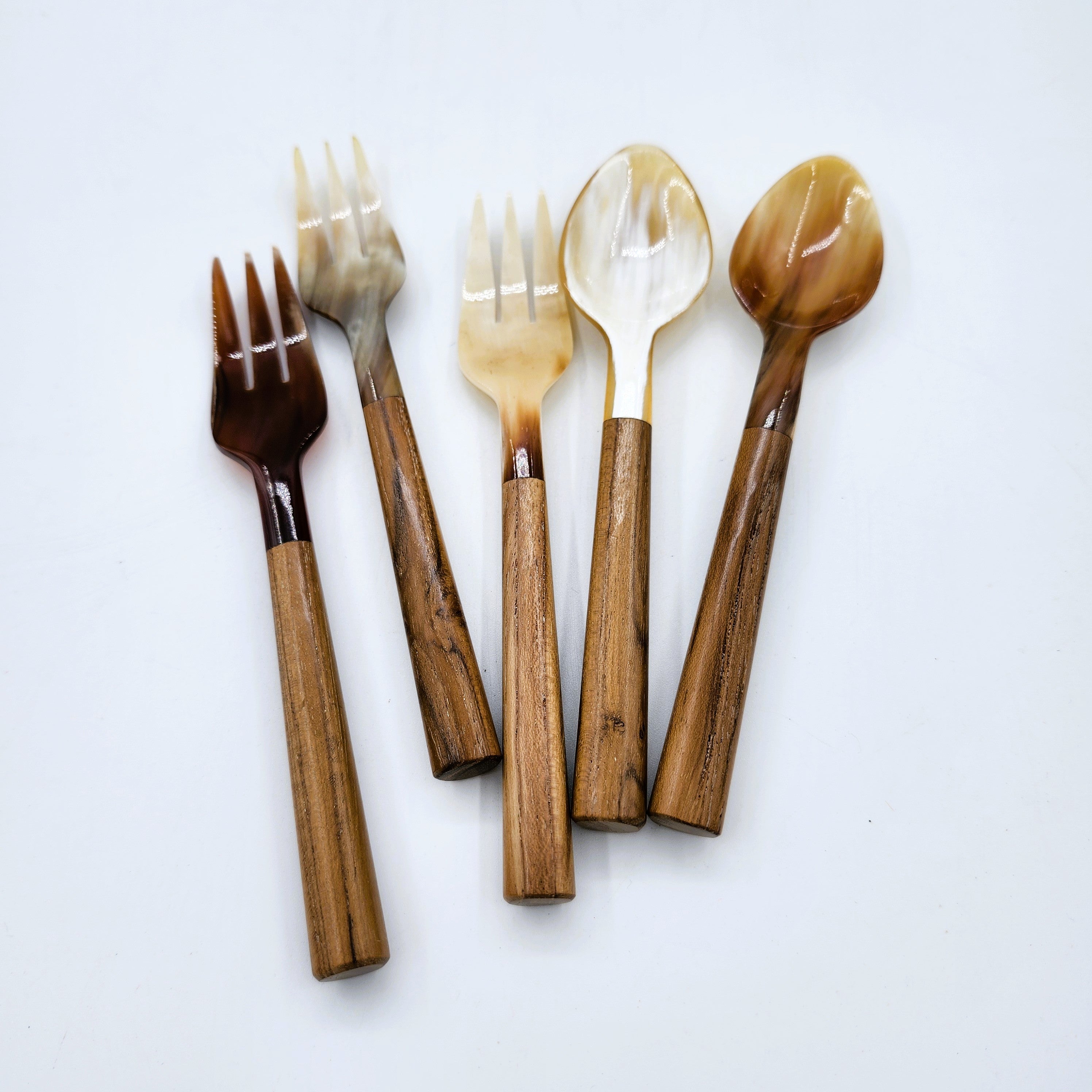 Five horn and wood pieces of cutlery, including three dessert forks, and two spoons, arranged on a plain white background.