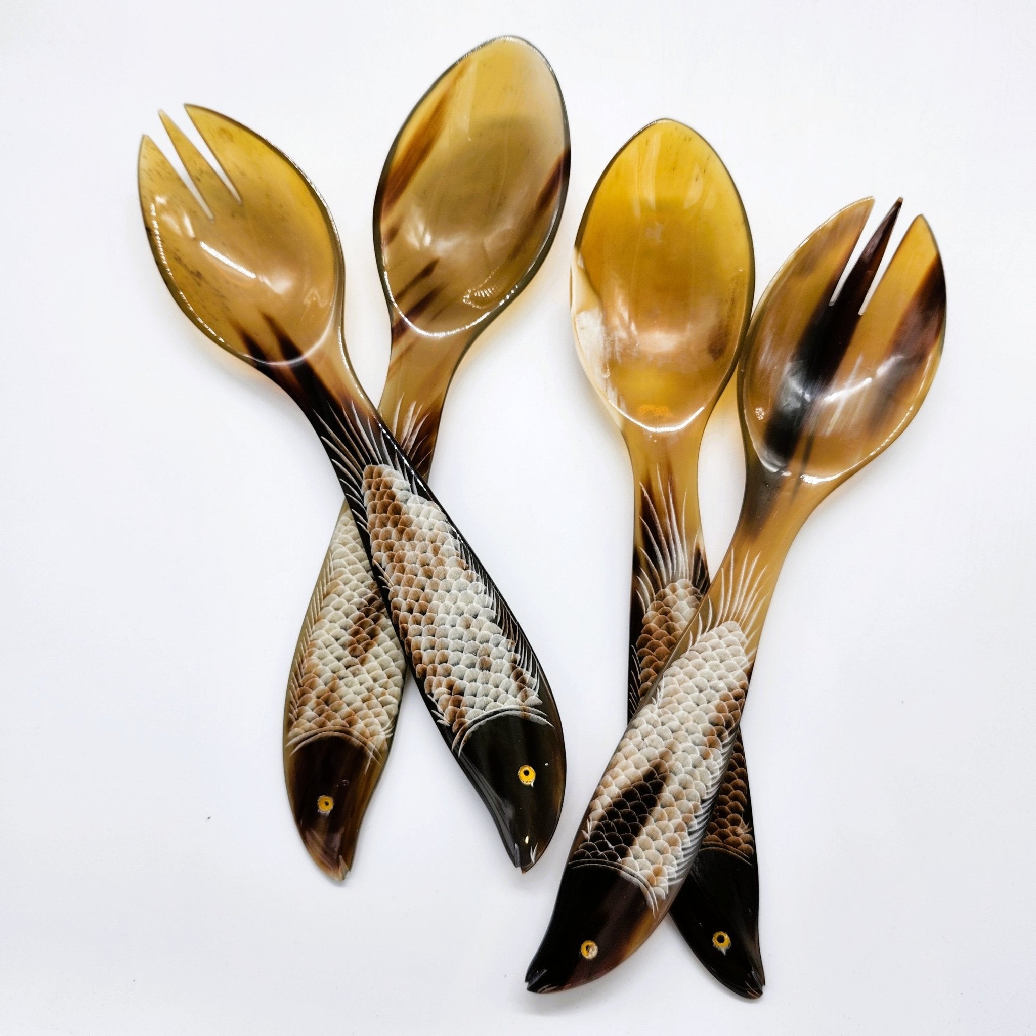 Two pairs of decorative fish-shaped salad servers, including two spoons and two forks, arranged on a plain white background. The handles are carved to resemble fish scales with dark heads and small gold eyes.