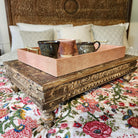 Styled view of the vintage teak bajot, a low carved platform from India that could be used as a tray table on a sofa or bed