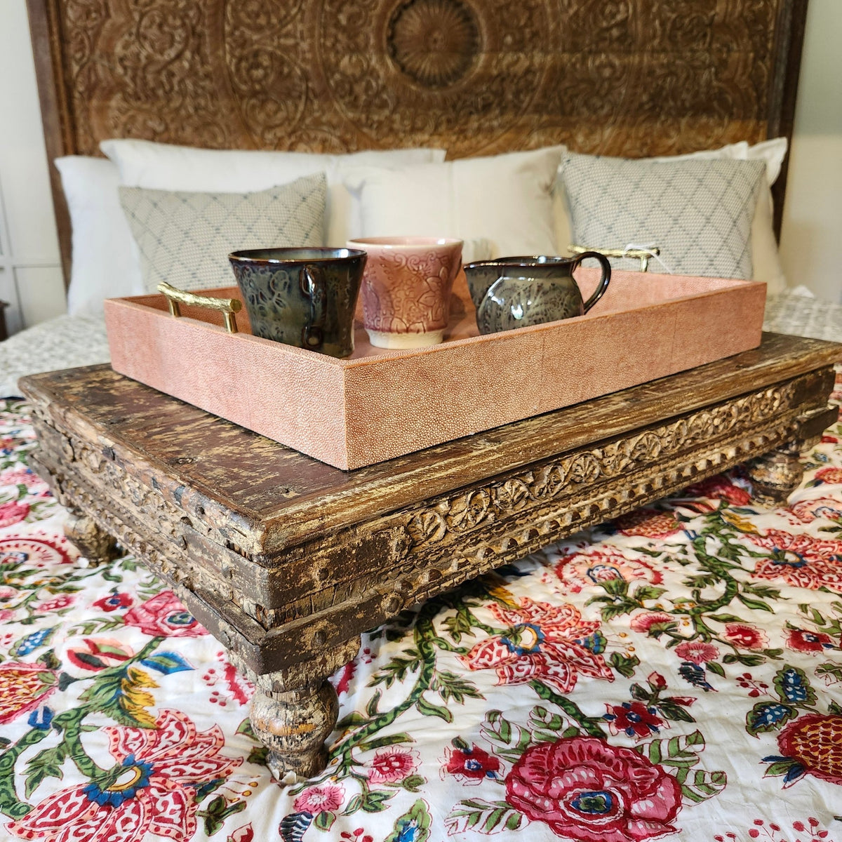 Styled view of the vintage teak bajot, a low carved platform from India that could be used as a tray table on a sofa or bed