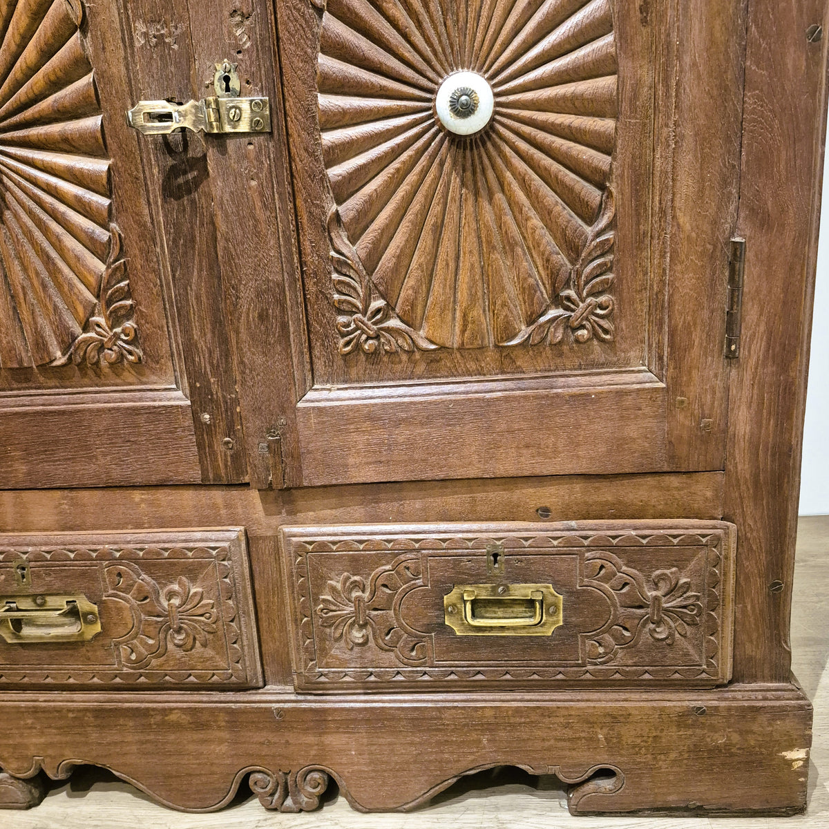 Elaborately carved sunburst detail on a four door teak cabinet from India, with ceramic knobs throughout