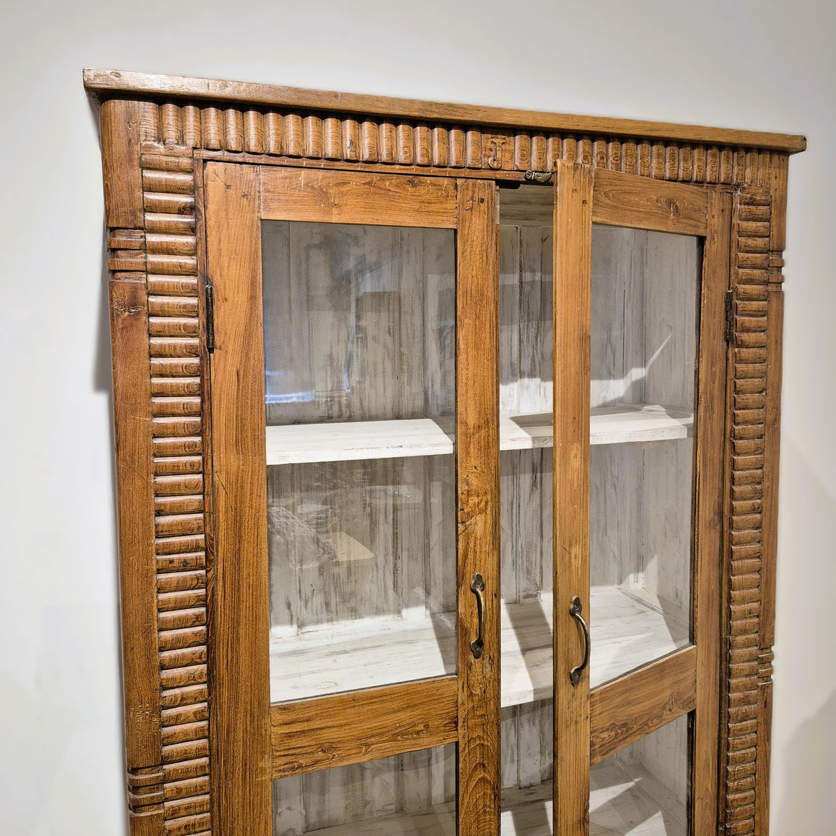 Hand carved fluting along the edge of a large vintage teak glass fronted cabinet, natural wax finish