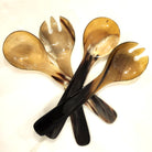 Four horn serving utensils, including two spoons and two forks, arranged in a crossed pattern on a plain white background.