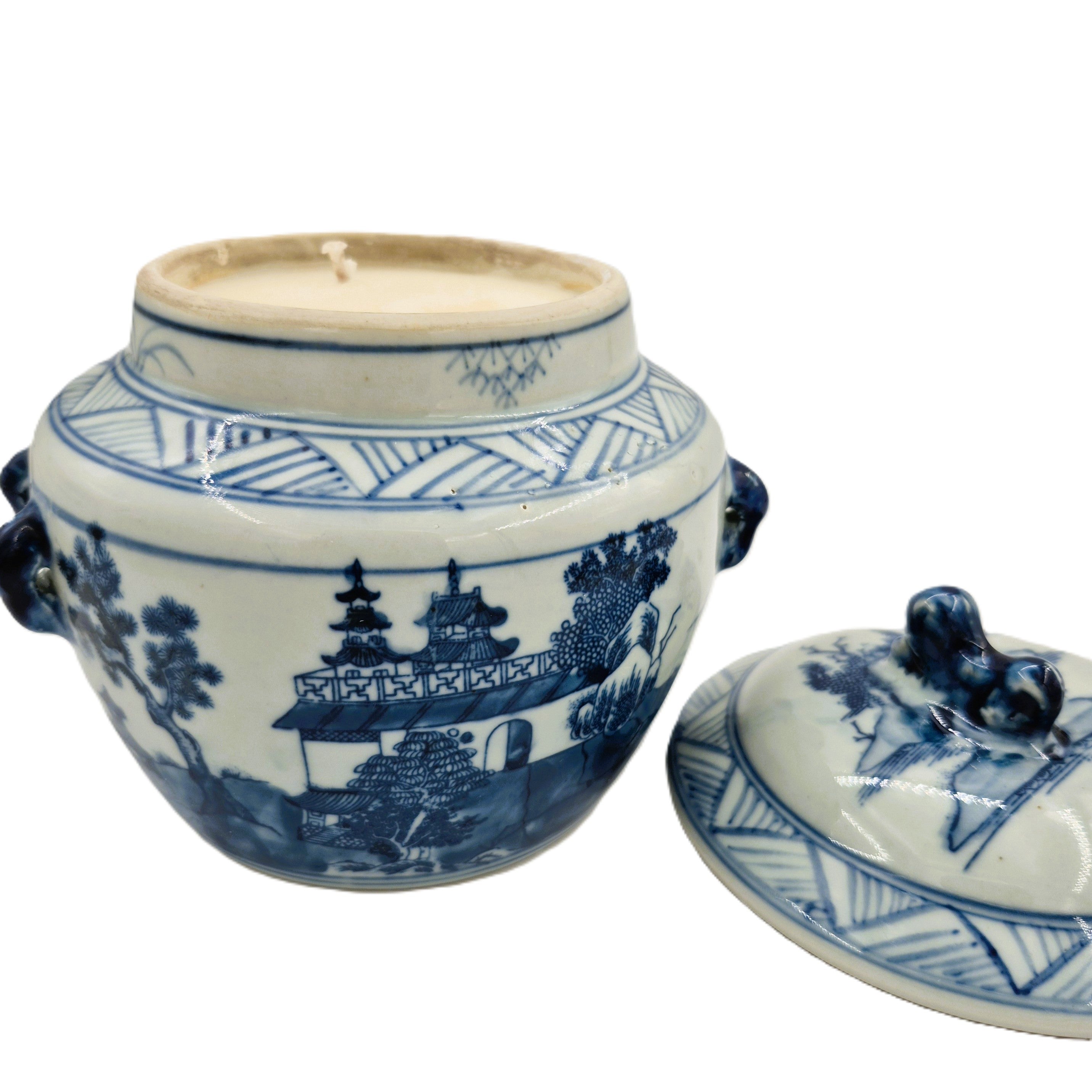 Blue and white ceramic jar with lid containing a scented candle on a white background