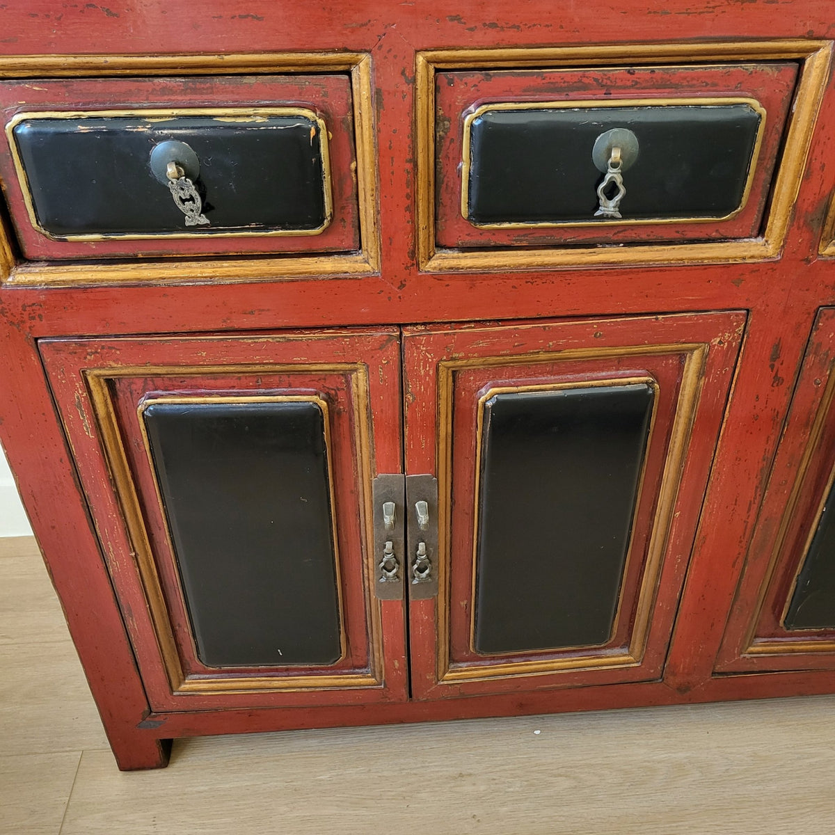 Detail of the red lacquer finish on a vintage Chinese sideboard, one of its six doors and six drawers shown at closer range