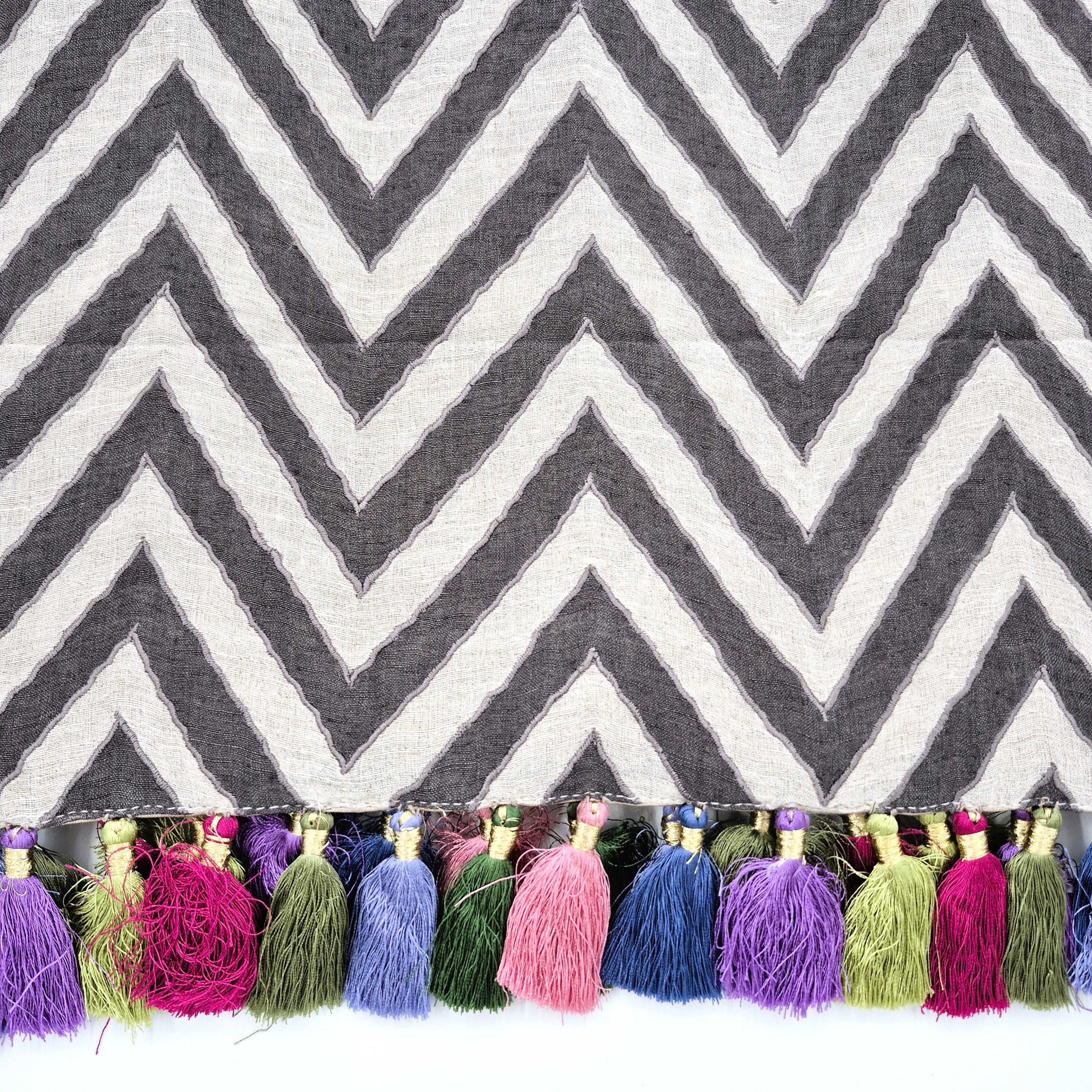 Chevron patterned linen table runner with colorful tassels on a white background