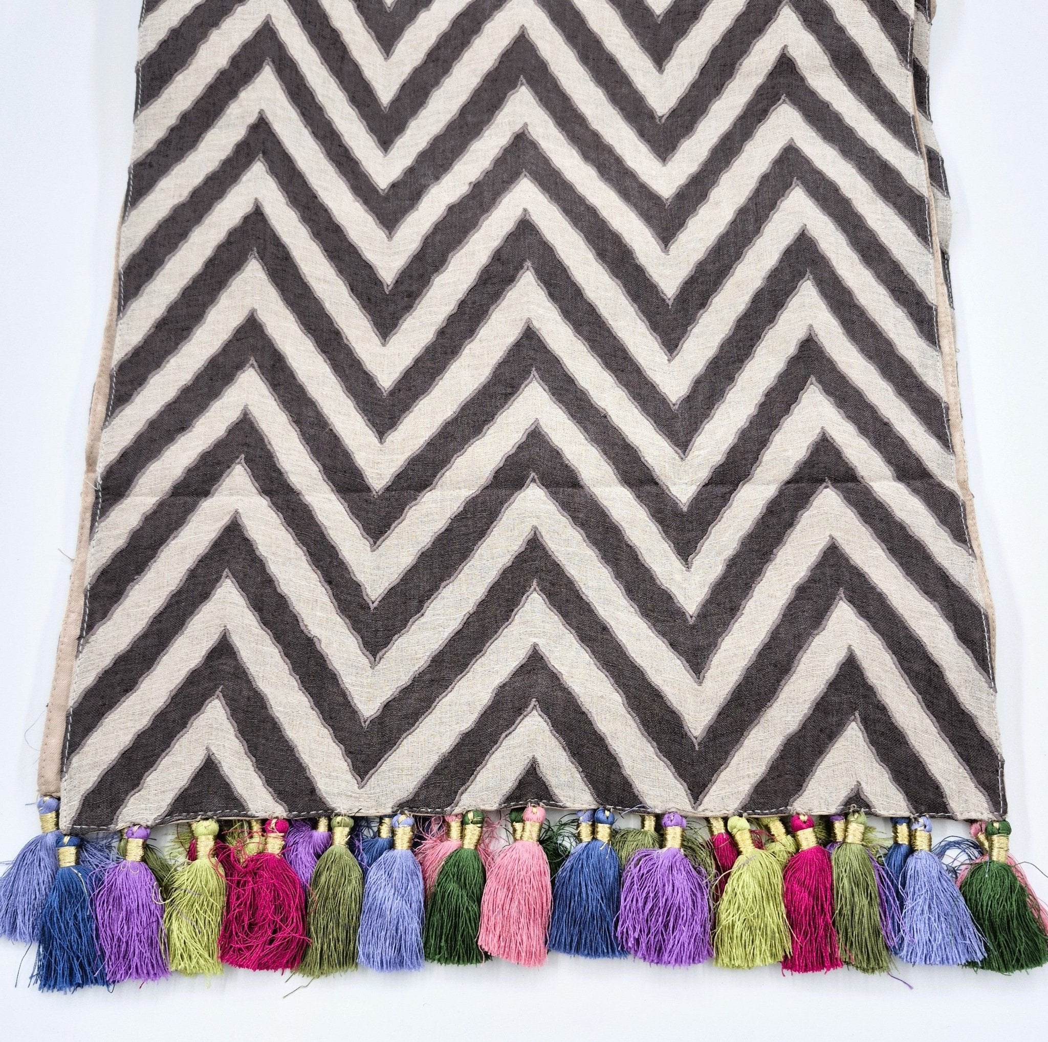 Chevron patterned linen table runner with colorful tassels on a white background