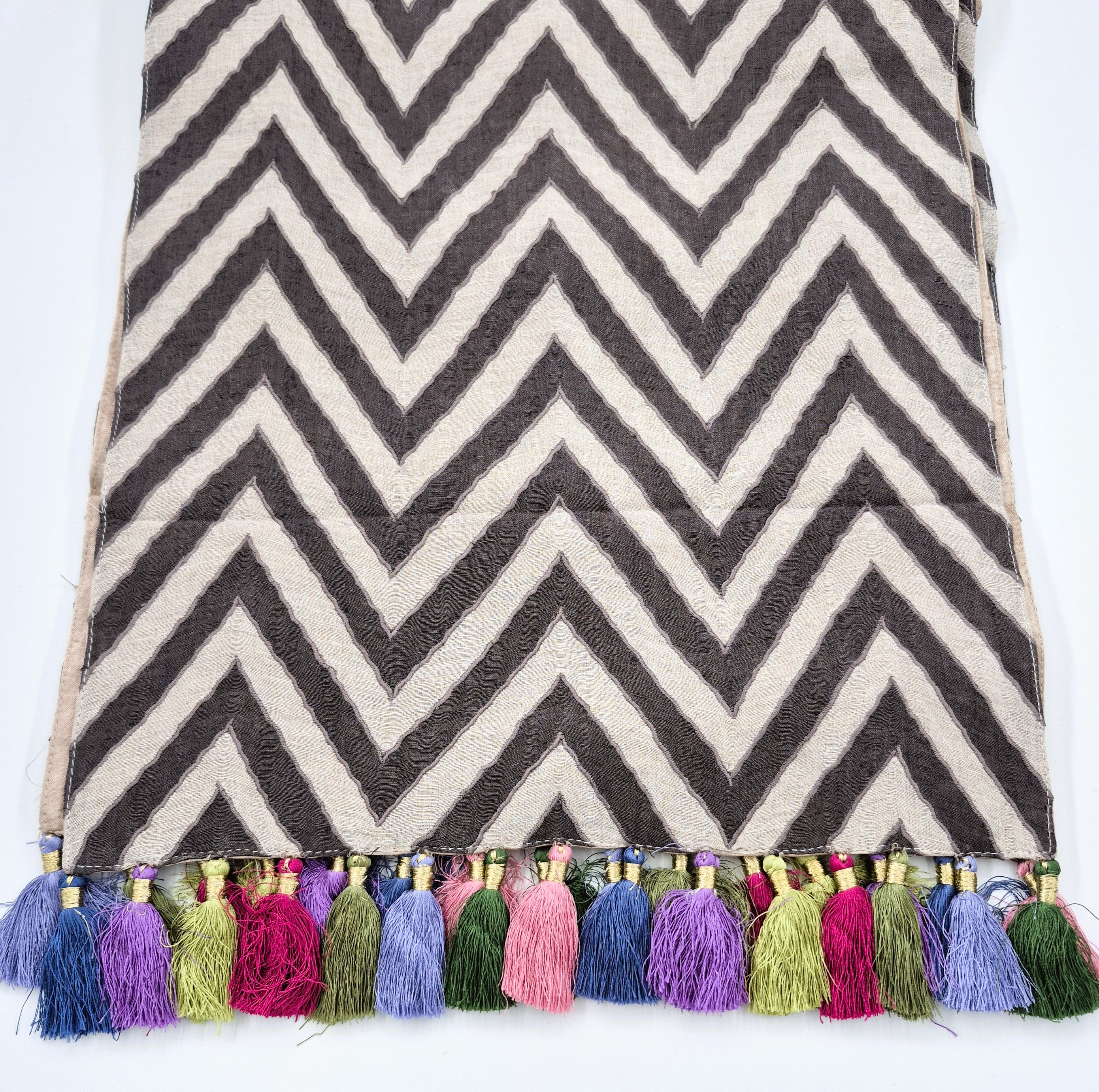 Chevron patterned linen table runner with colorful tassels on a white background