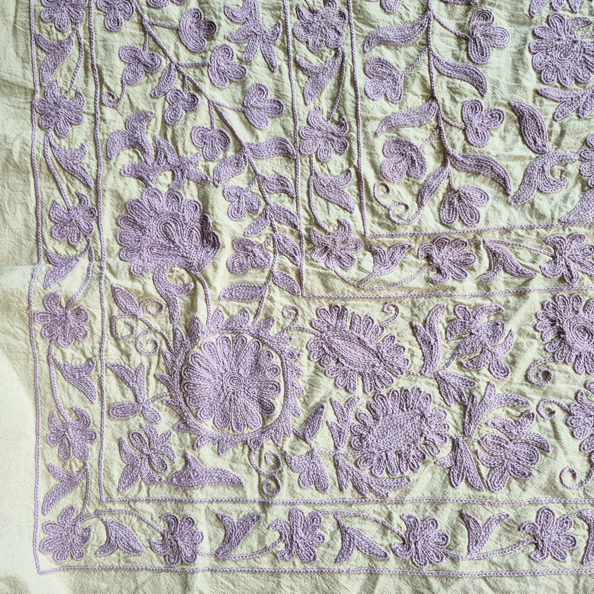 Suzani throw hand embroidered in lavender on a pale green cotton base, used as a tablecloth or bedcover