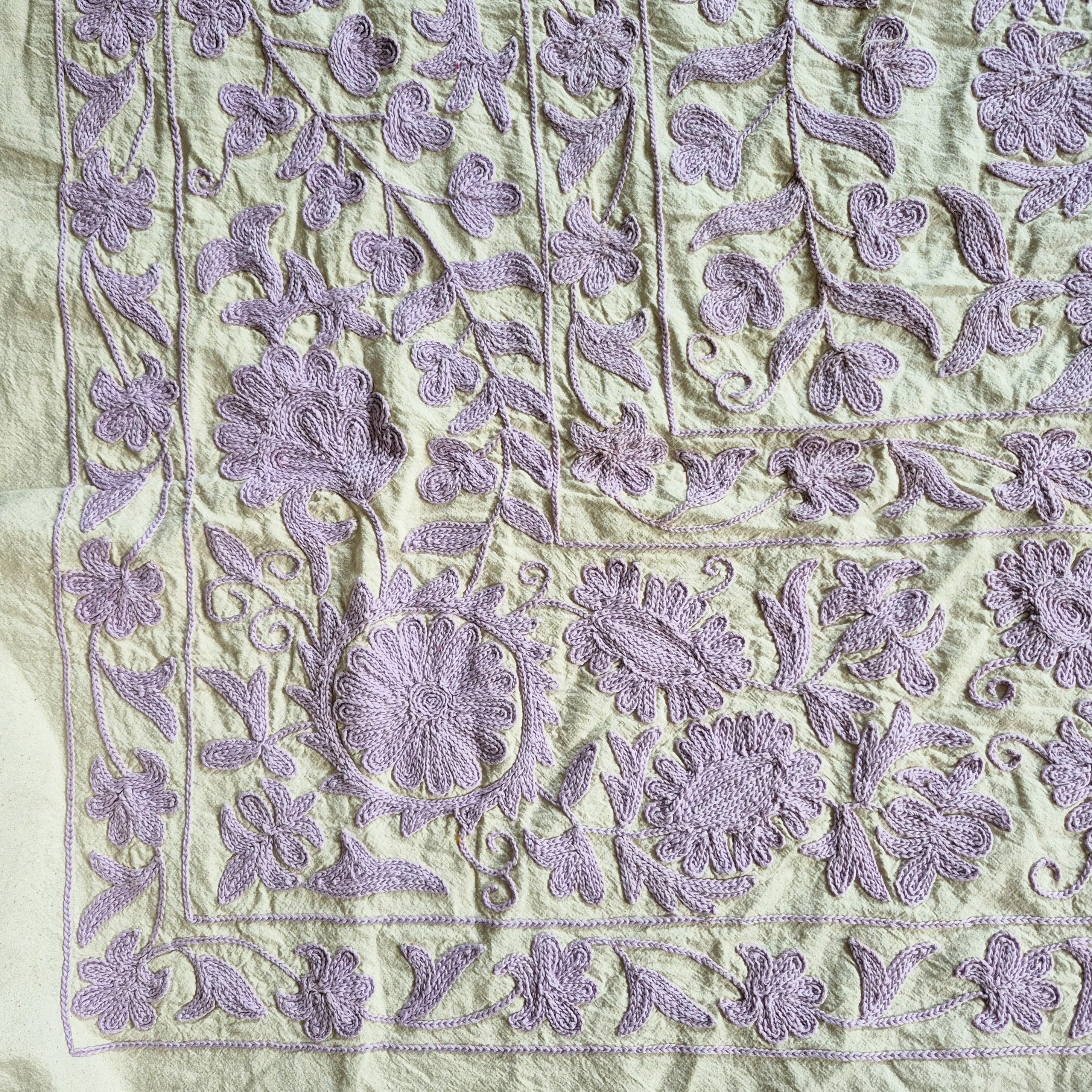 Suzani throw hand embroidered in lavender on a pale green cotton base, used as a tablecloth or bedcover