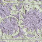 Detail of suzani throw showing lavender hand embroidery on a pale green cotton base, embroidered in India