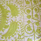 Close-up of lime green hand embroidered pattern on a cream fabric background.  Suzani.