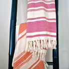 Striped towels in pink and orange draped over a towel ladder against a white background.